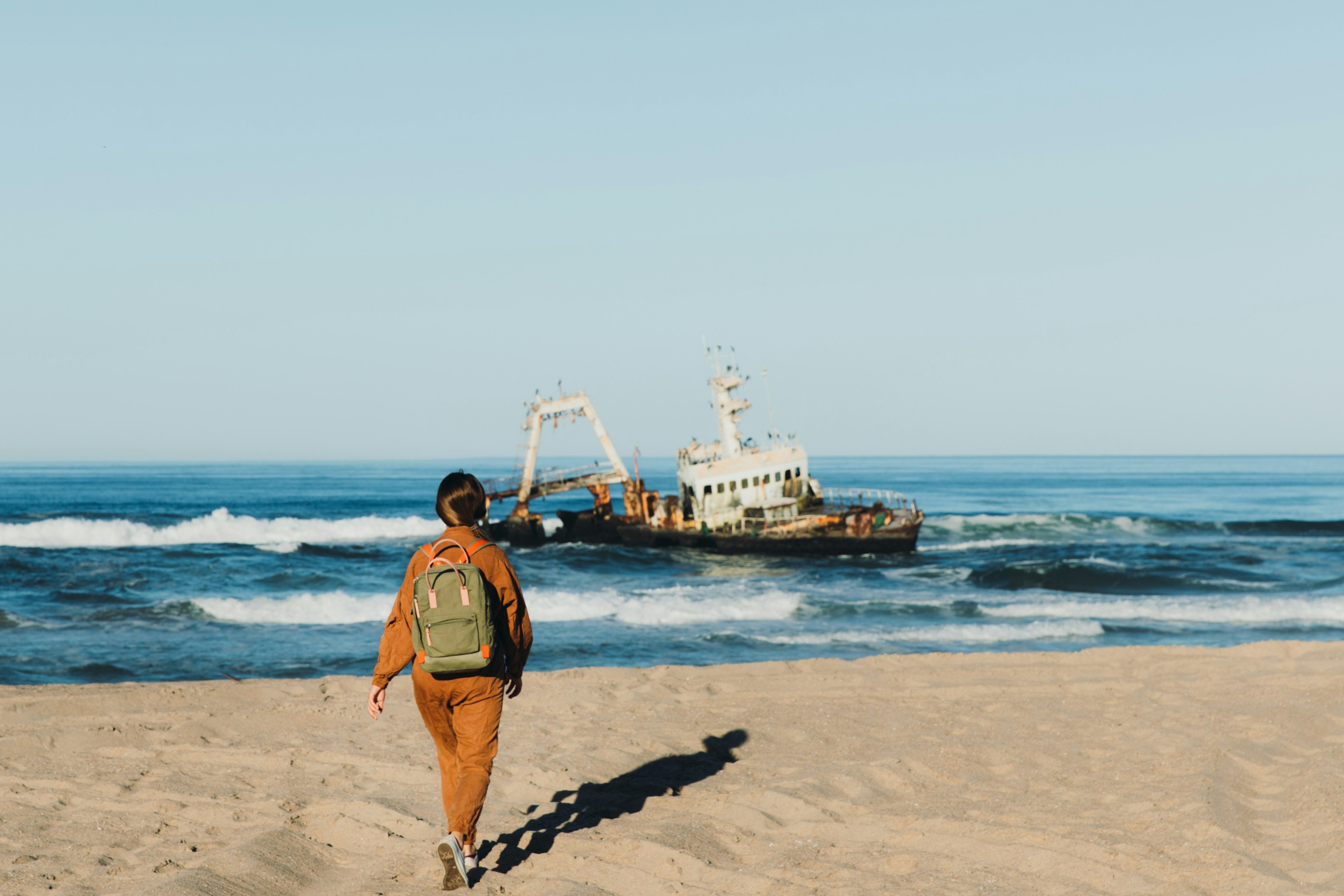 Young woman with backpack looking at an abandoned ship on the Skeleton Coast in Namibia