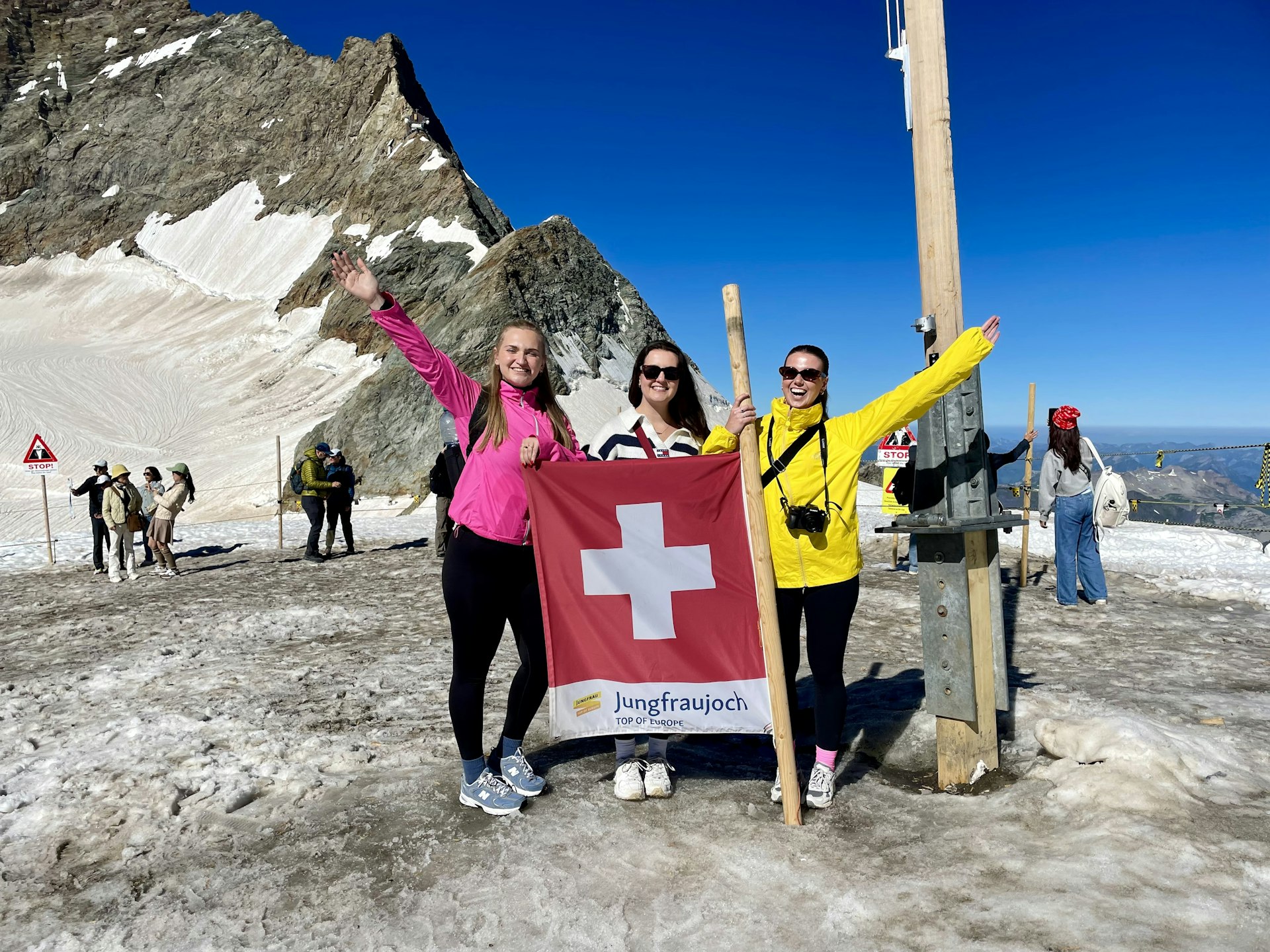 Three women standing on an alpine peak holding a Swiss flag