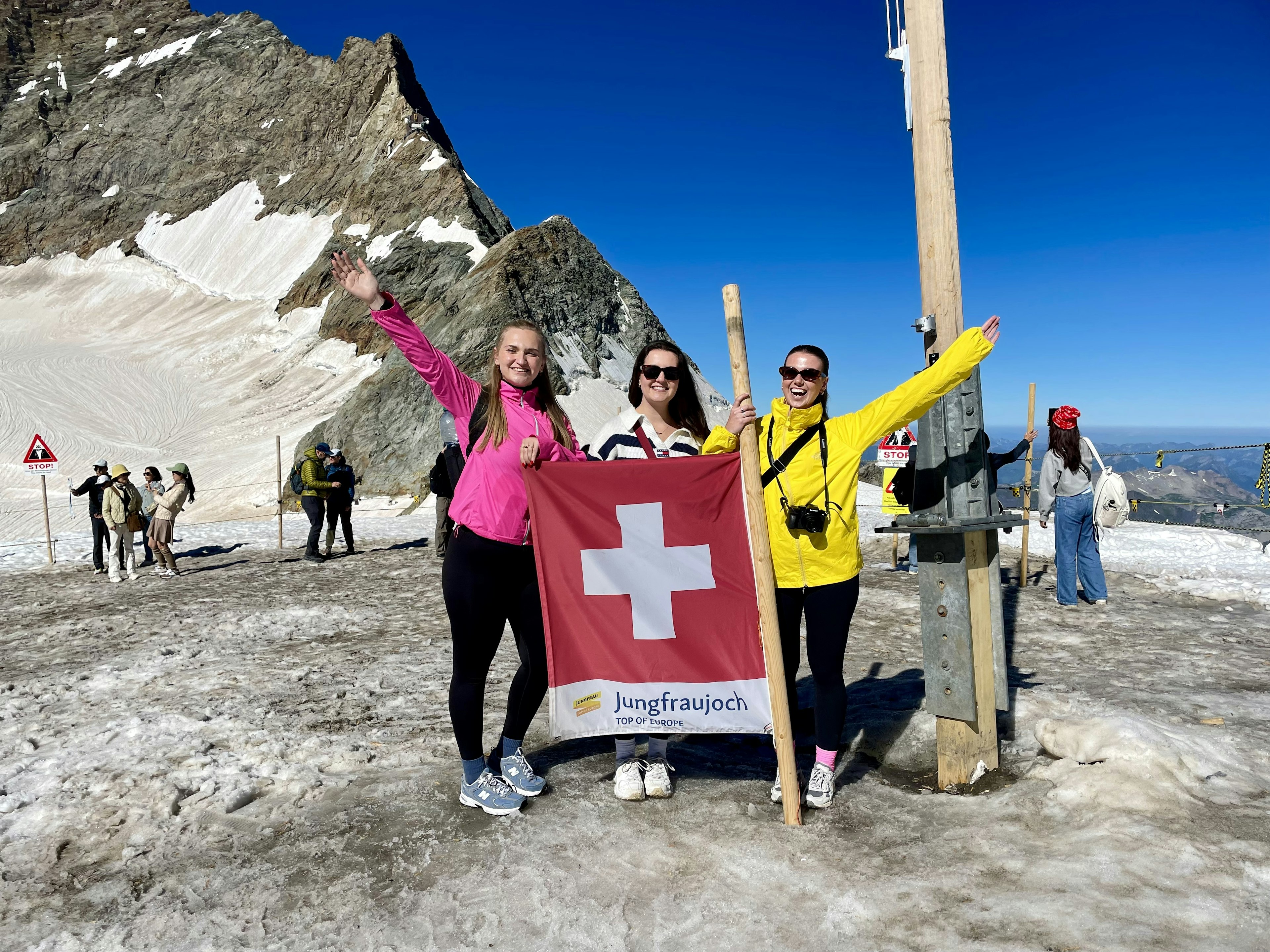 Three women standing on an alpine peak holding a Swiss flag