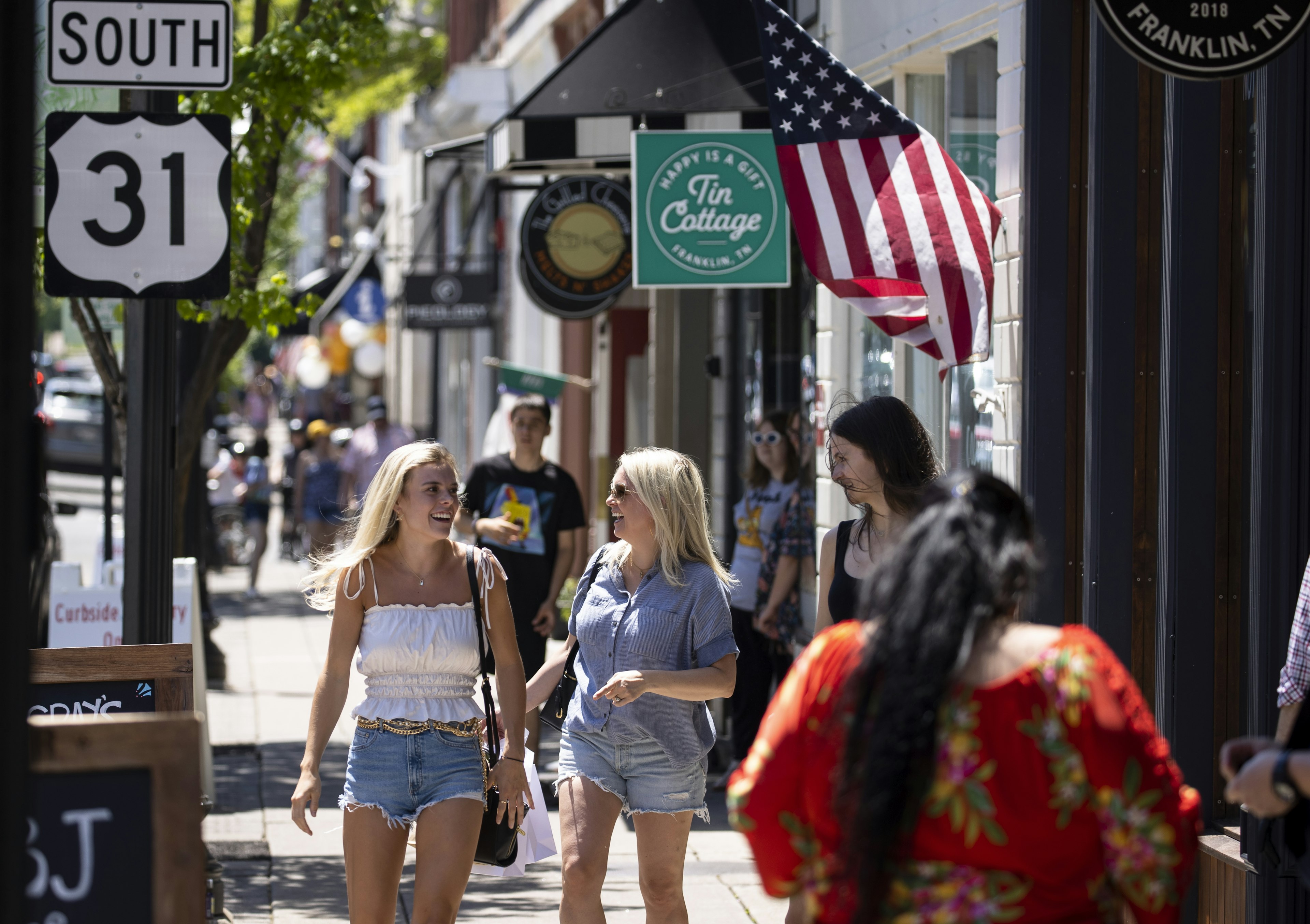 Two white women laugh together as they walk down a street