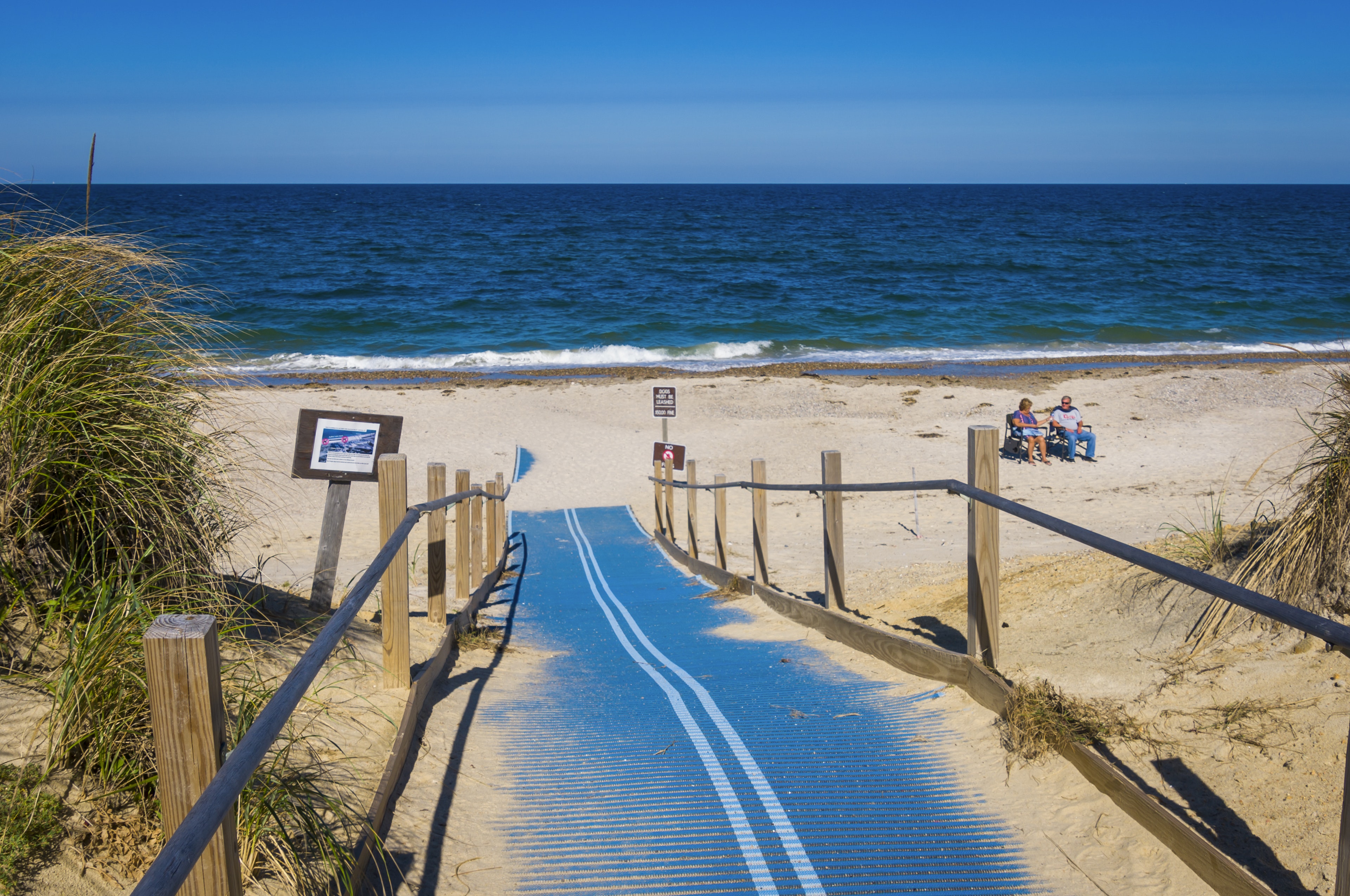 A mature couple enjoys a near-empty beach in  Sandy Neck Reservation. There is an accessible ramp leading to the beach.