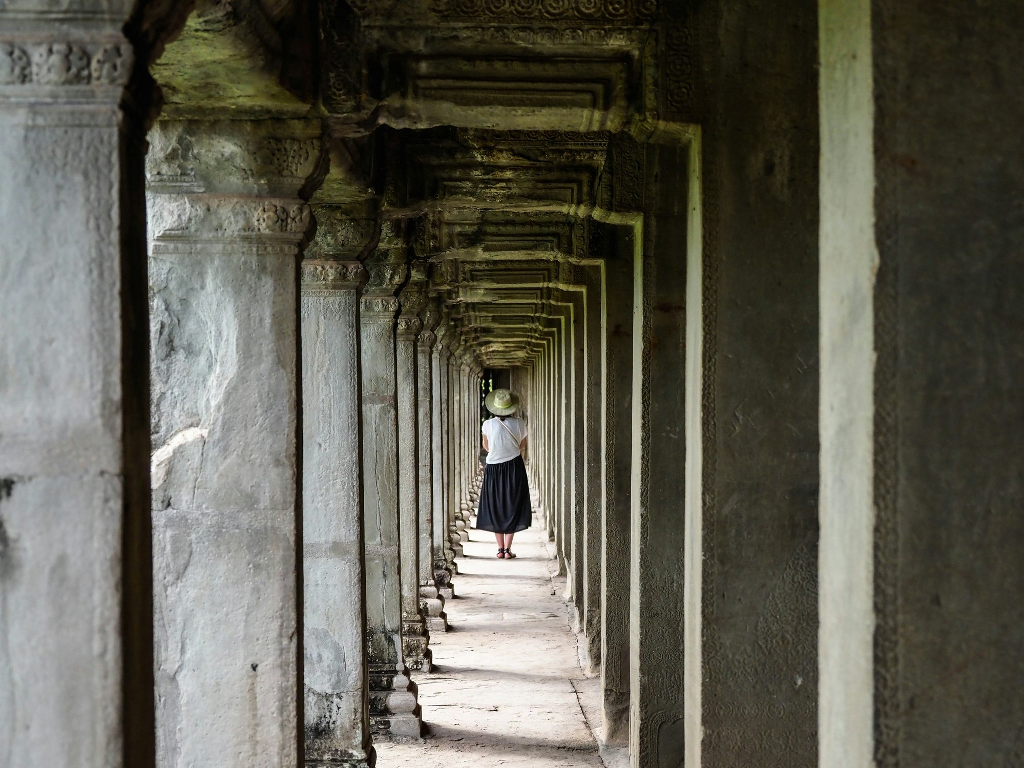 A woman walking along a corridor of stone columns at Angkor Wat.