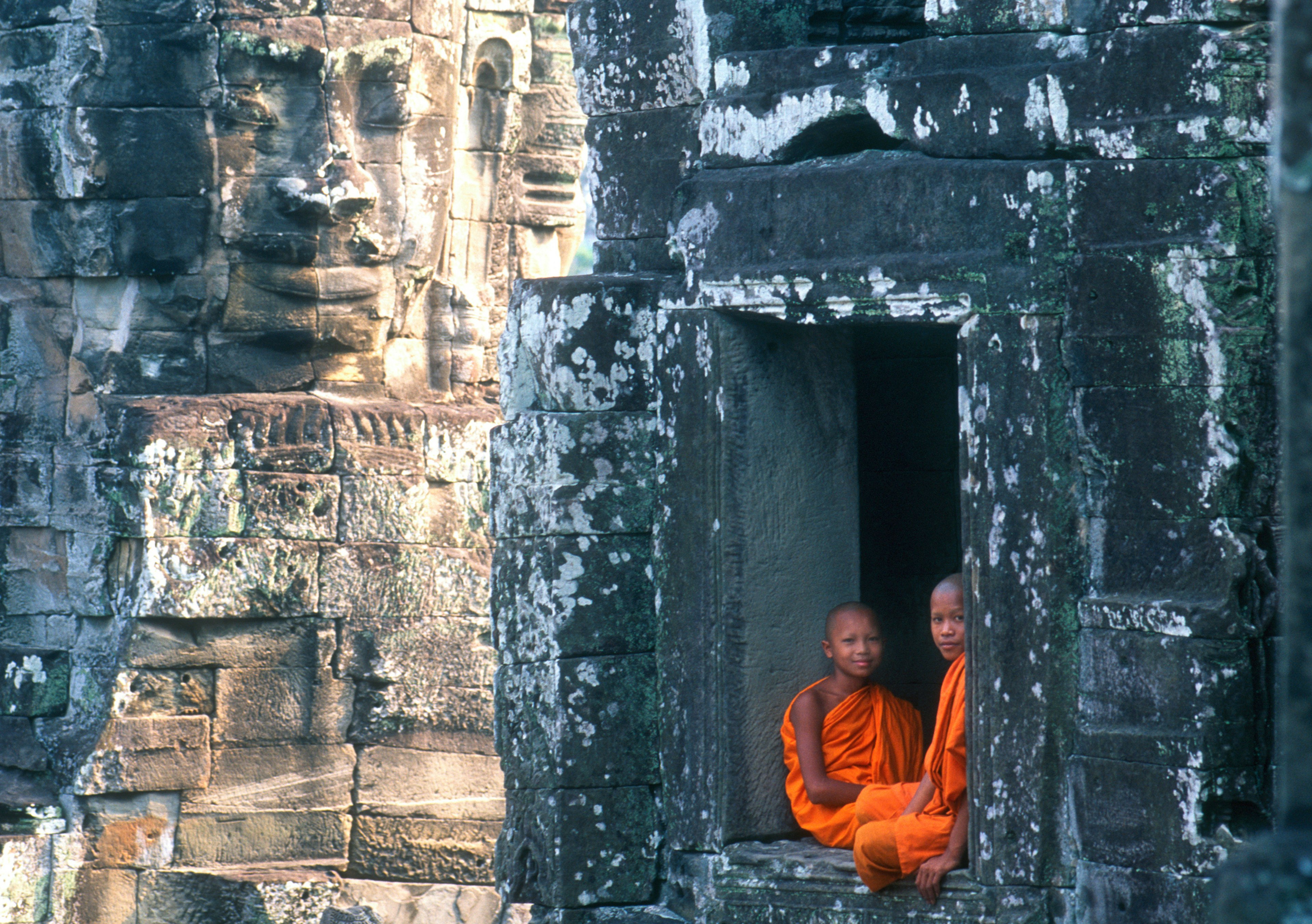 Two Cambodian monks in orange robes sit in a huge space in a wall in Angkor Wat