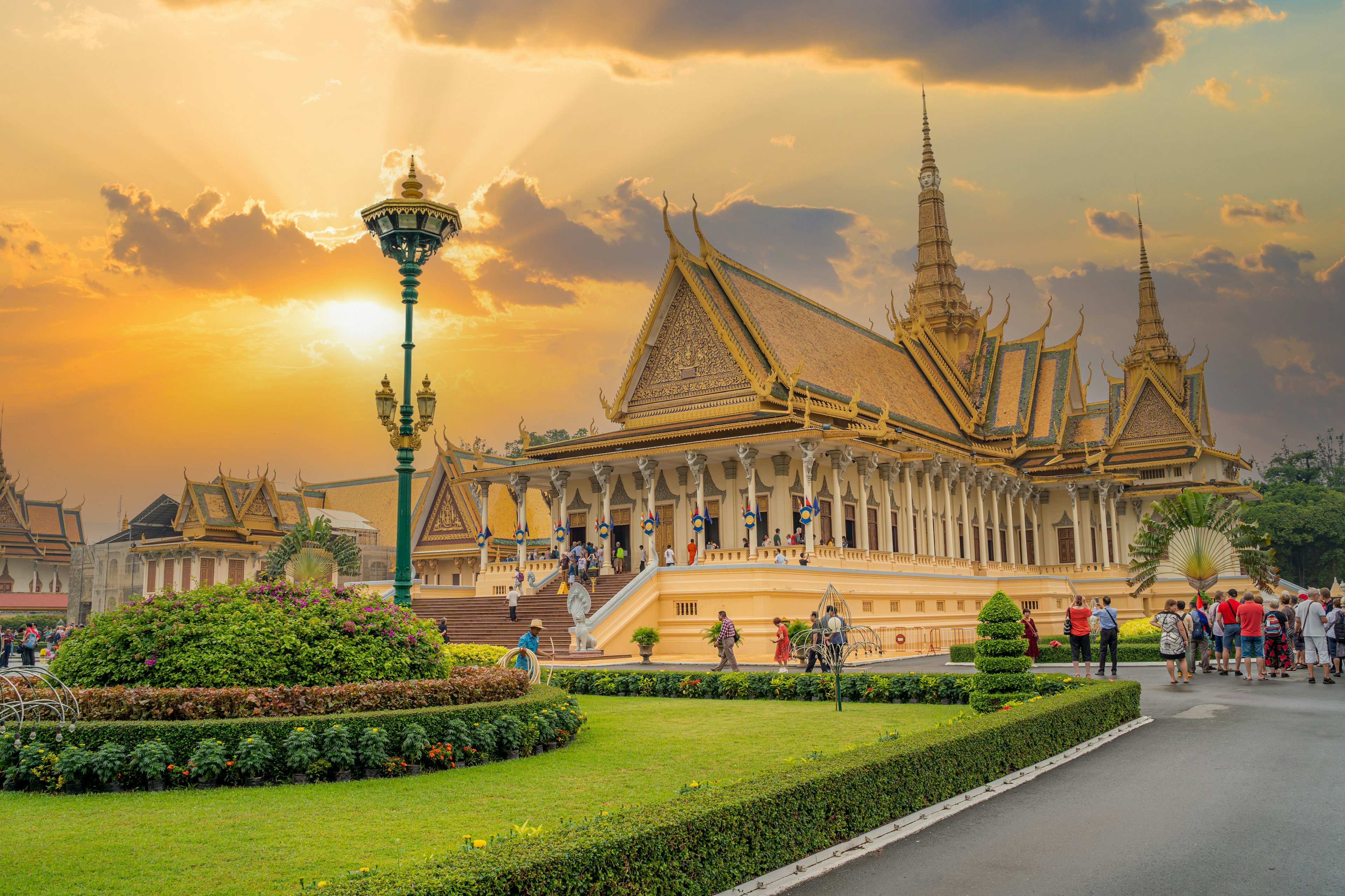 A temple appears golden in the sunlight. Several tourists are milling around the manicured grounds