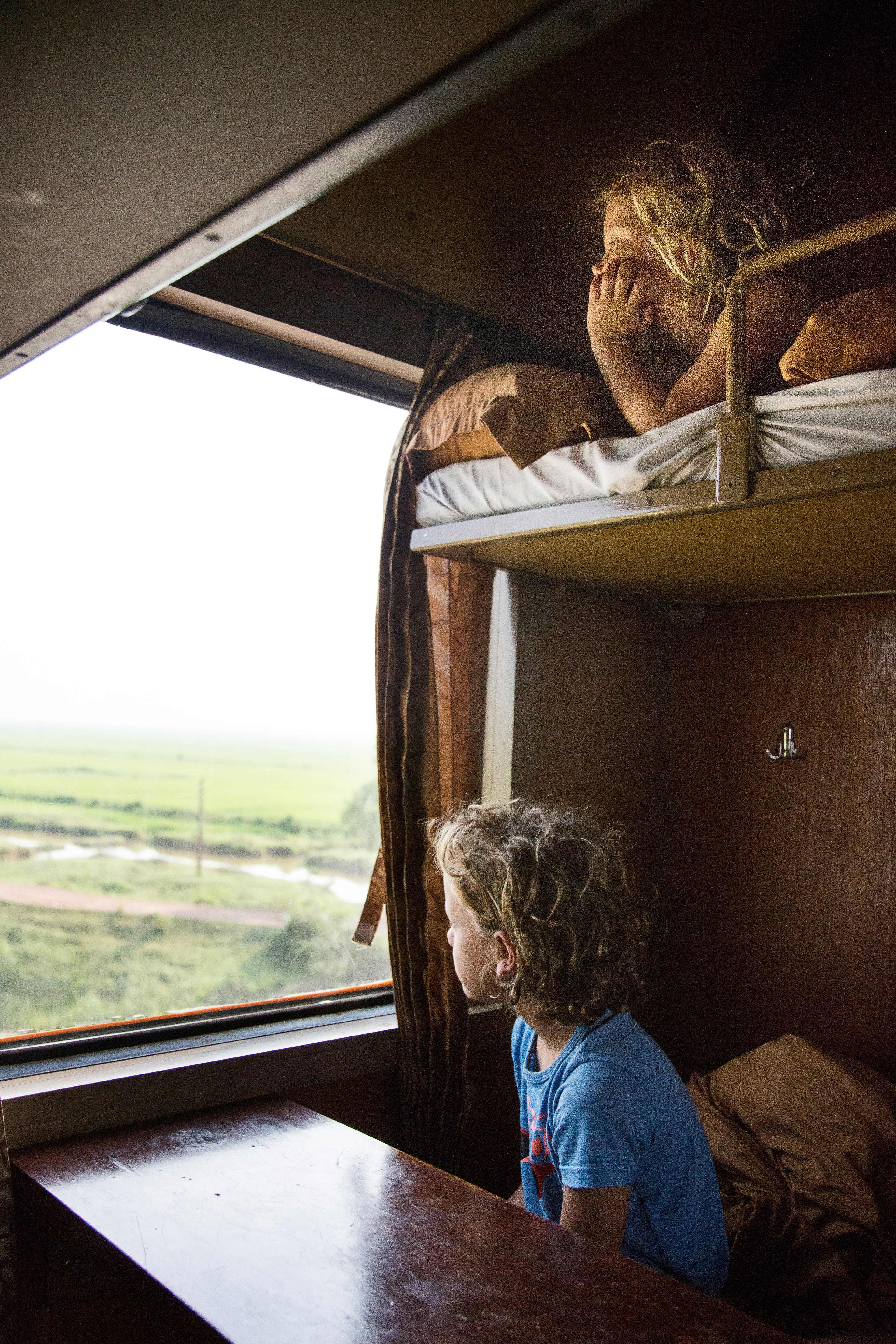 A brother and sister look out of a train window on a sleeper train