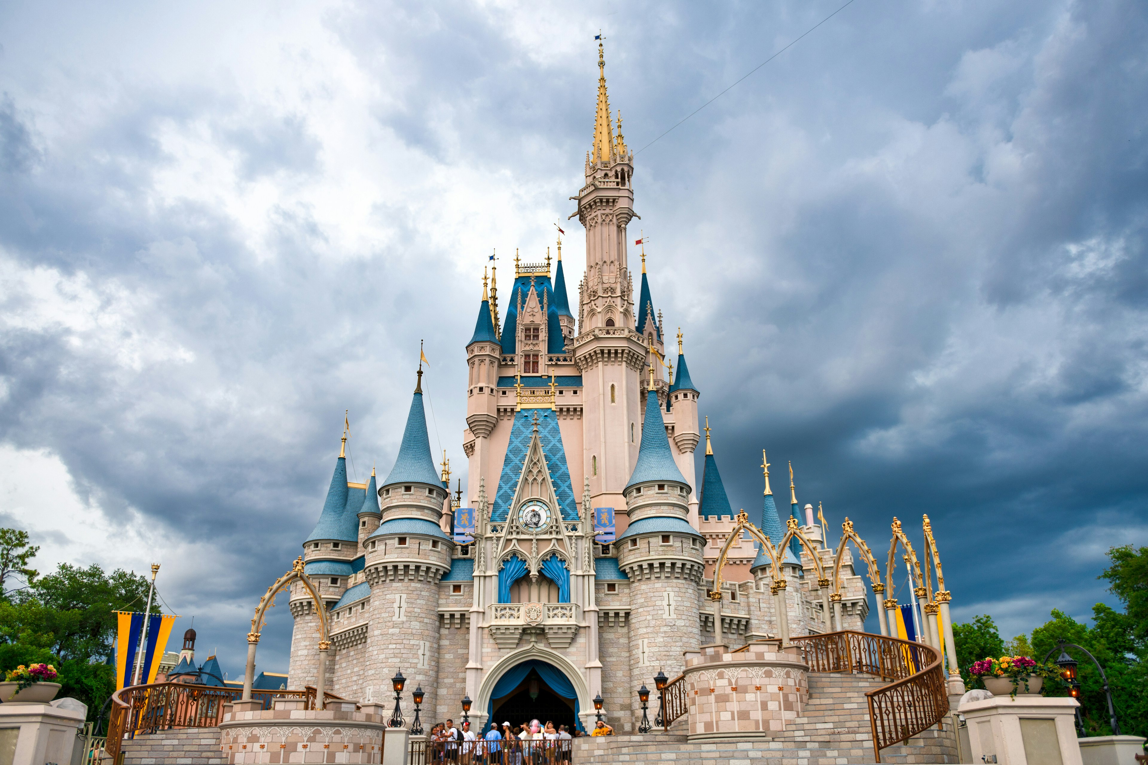 People gather at the arched entrance to a many-turreted pale pink castle