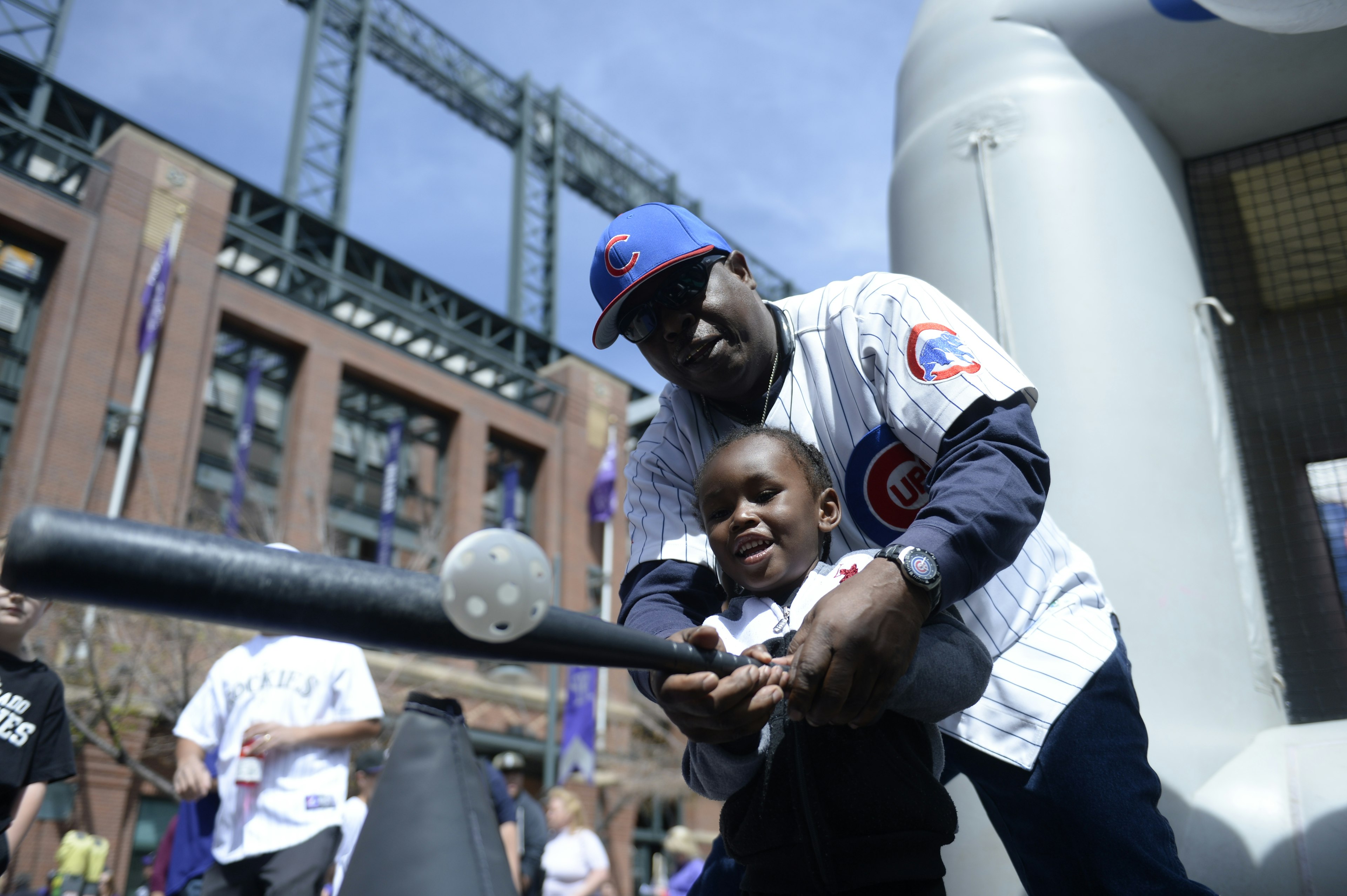 A young boy swings a baseball bat with the help of his grandfather outside Coors Field in Denver, Colorado