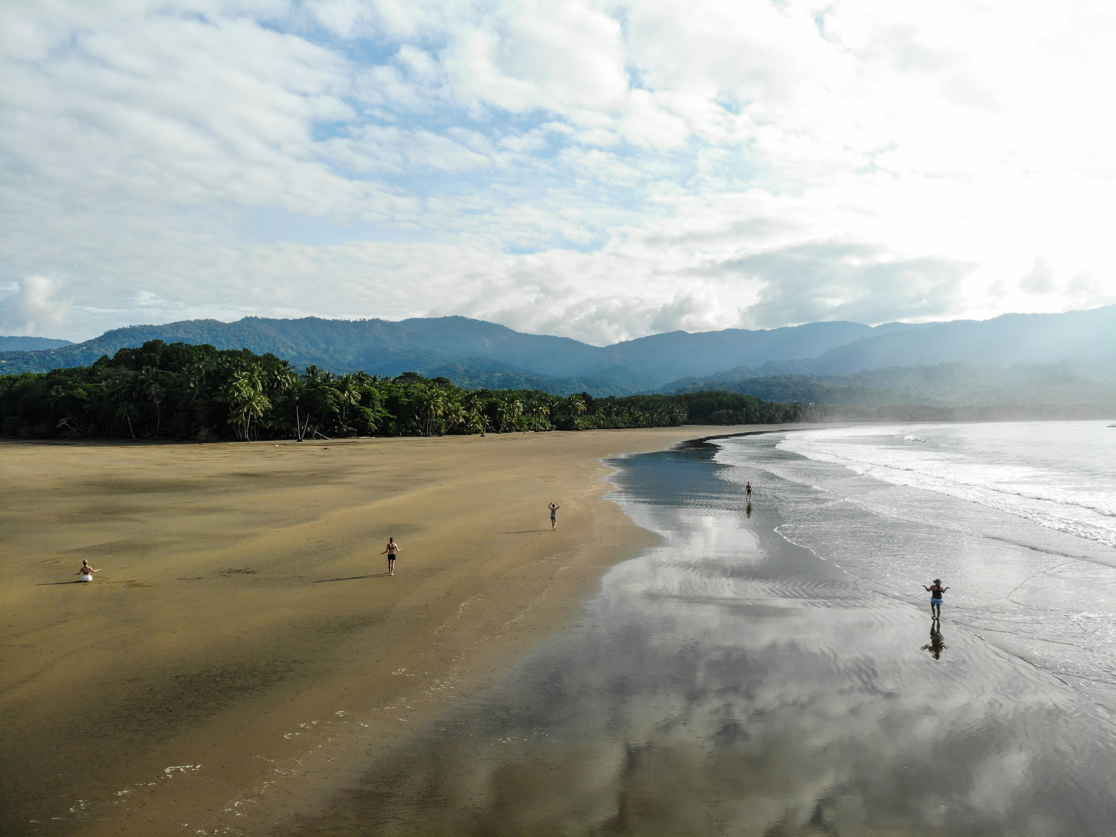 A small group of people in yoga poses make the most of the space on an empty beach