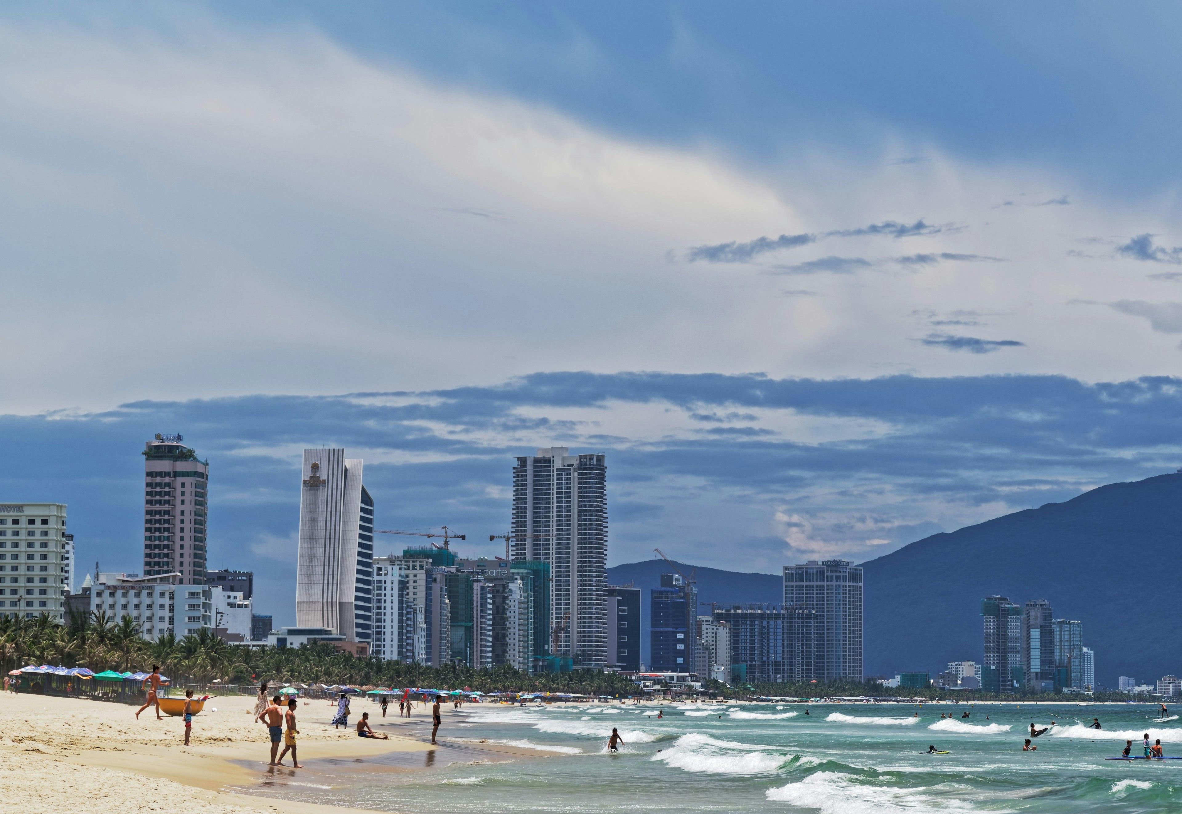 View of the seafront high-rise hotels behind sandy My Khe beach in Da Nang, Vietnam. Many people are on the beach or swimming in the sea.