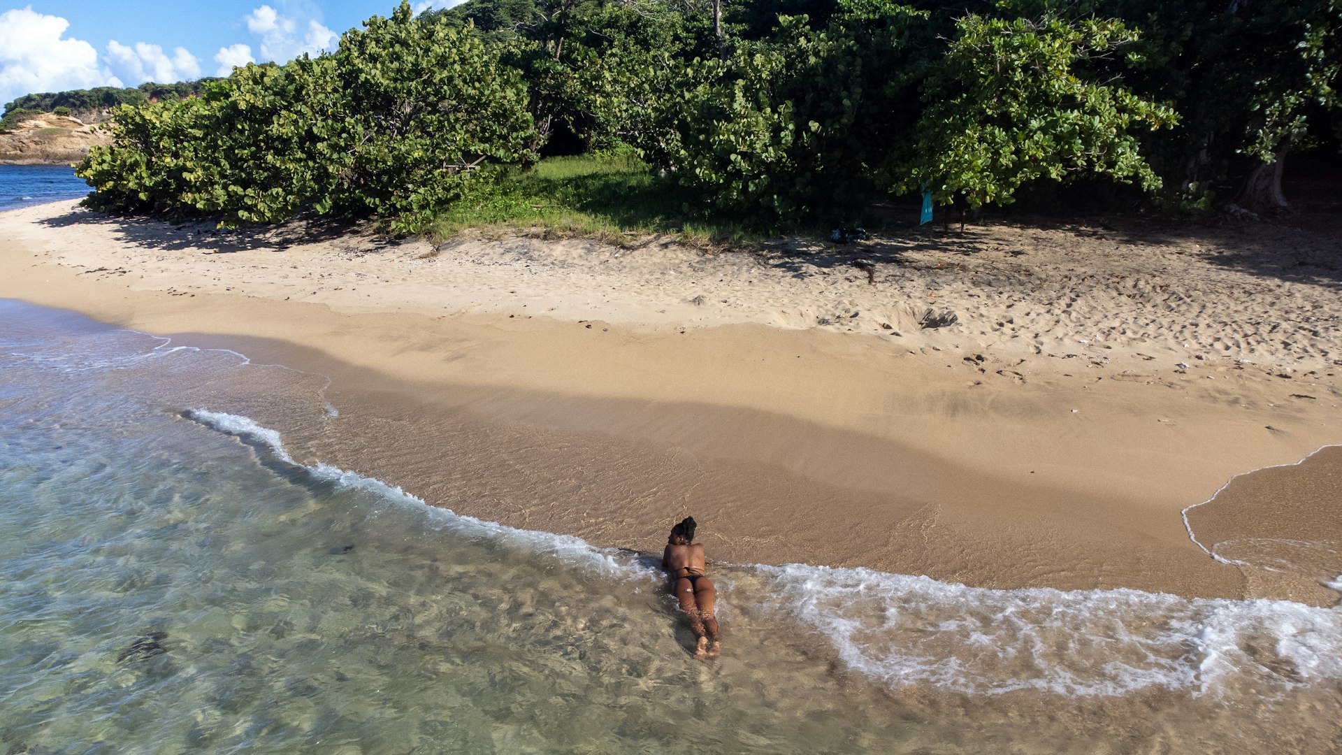 A woman lounges on her stomach on the sands of Point Baptiste Beach as the waves lap her body, Dominica