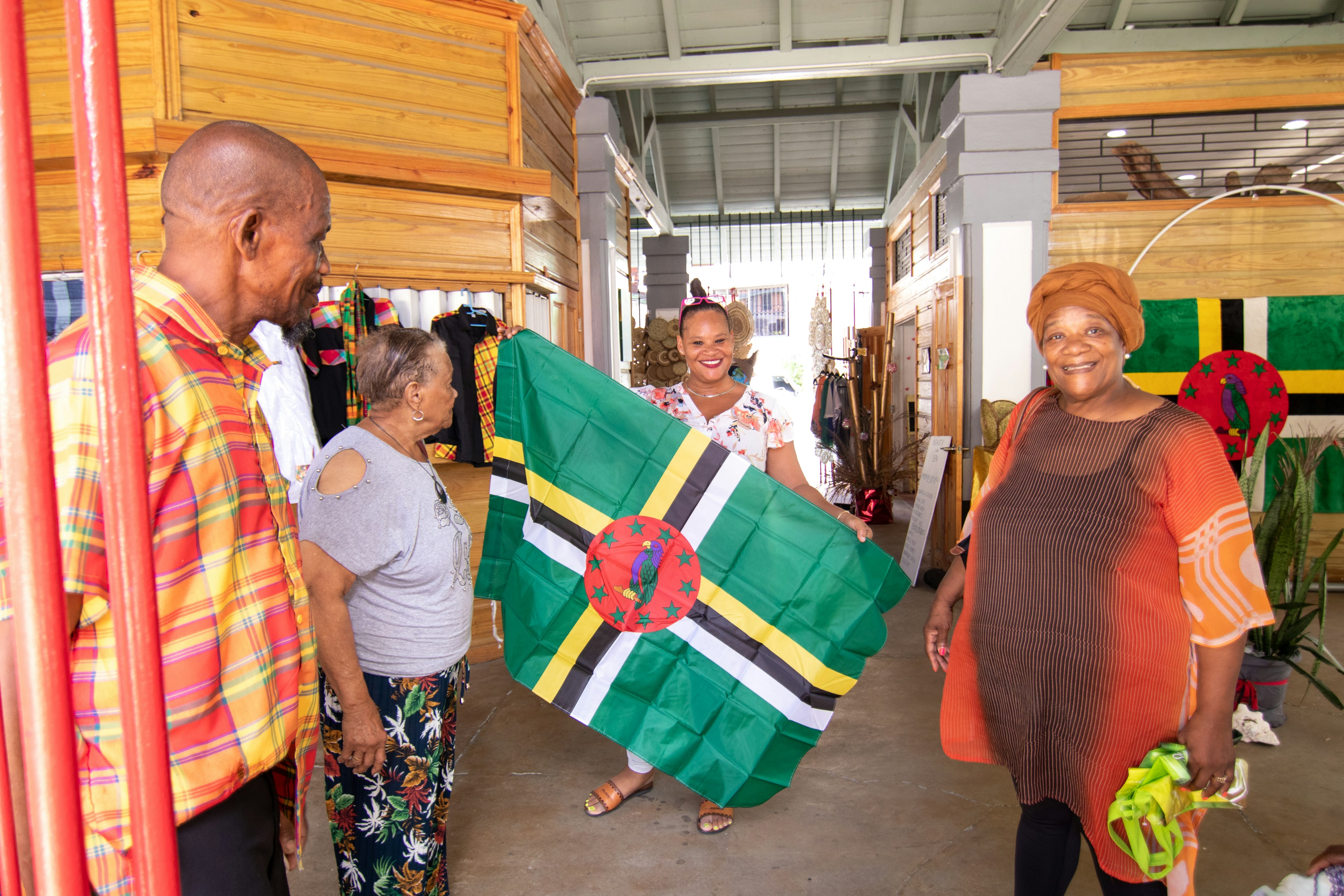 A woman holds up a Dominican flag with other people and vendors at the Old Market in Roseau, Dominica