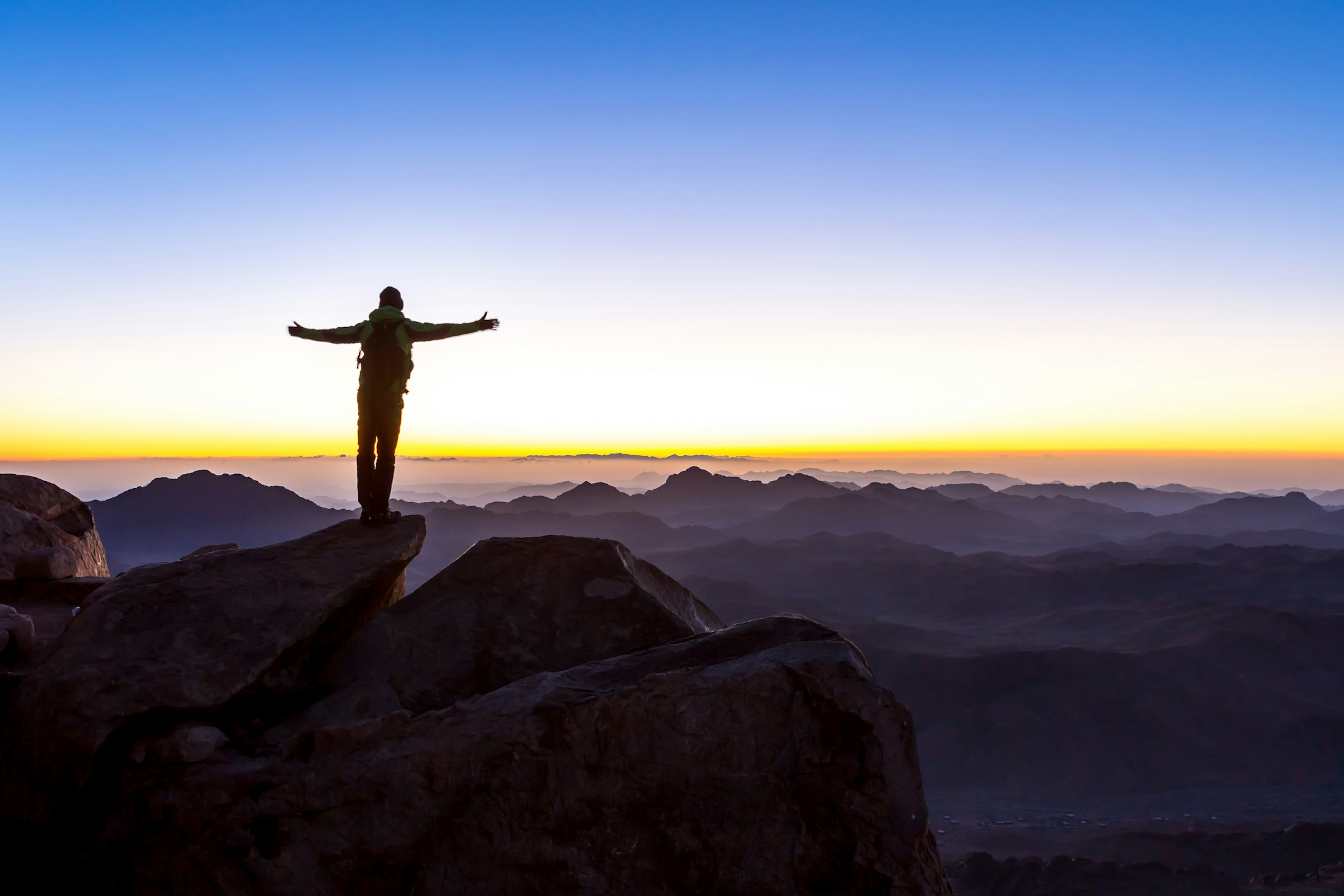 A man stands with open arms at the summit of Mount Sinai, Mount Moses in Egypt, Africa at sunrise