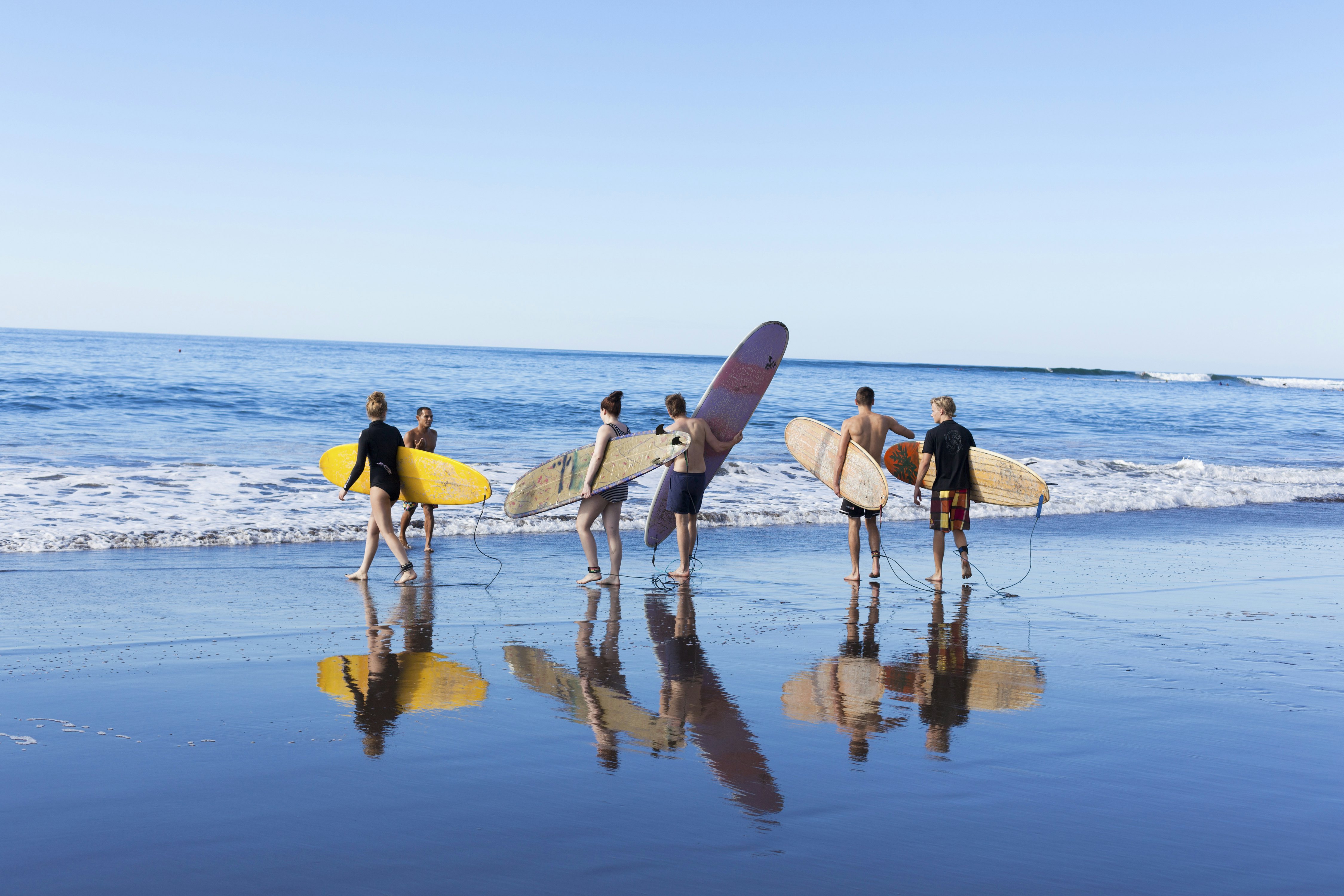 Six surfers carrying boards make their way into the ocean