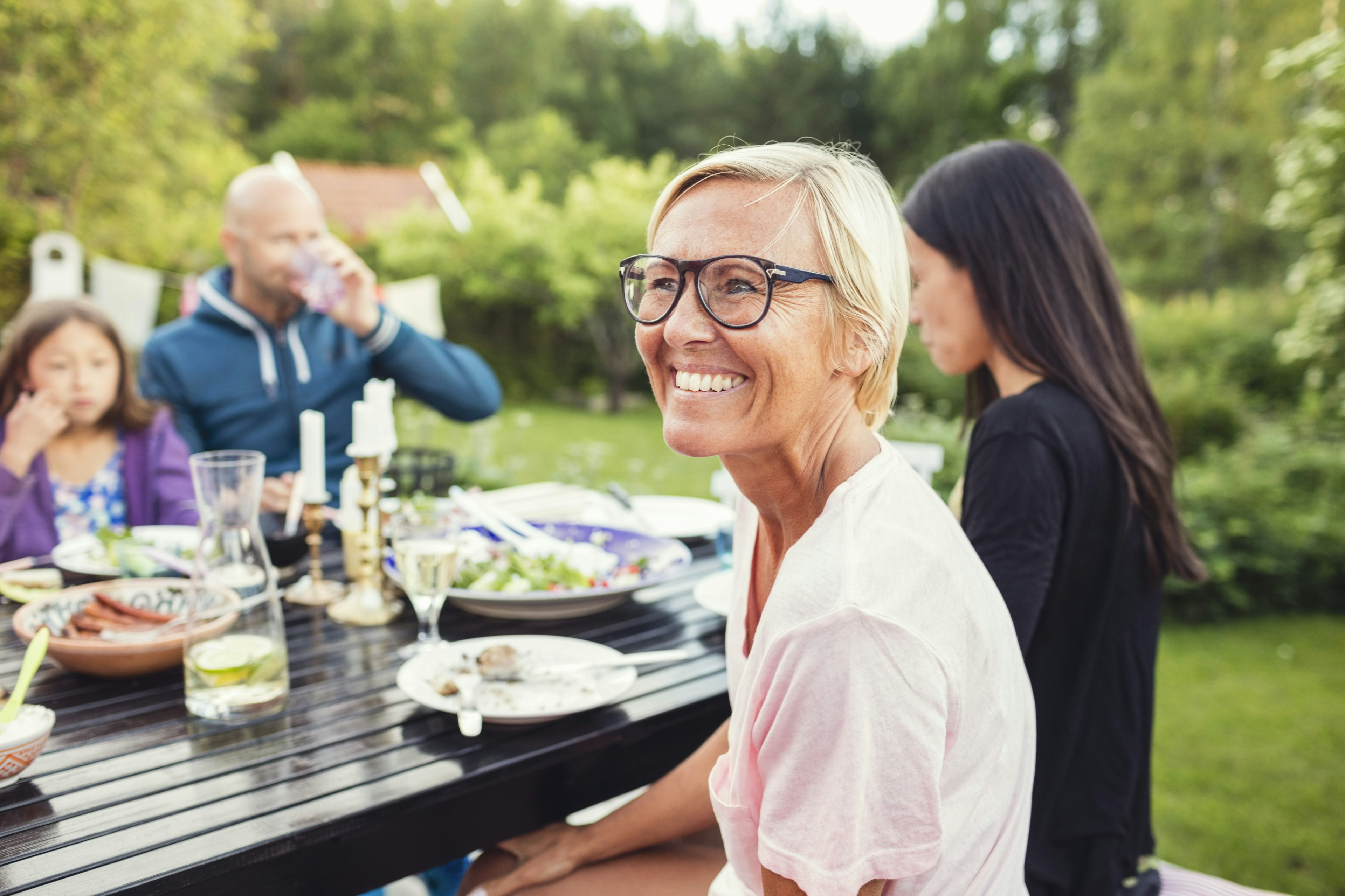 Happy woman sitting with friends and family at dining table in back yard during garden party