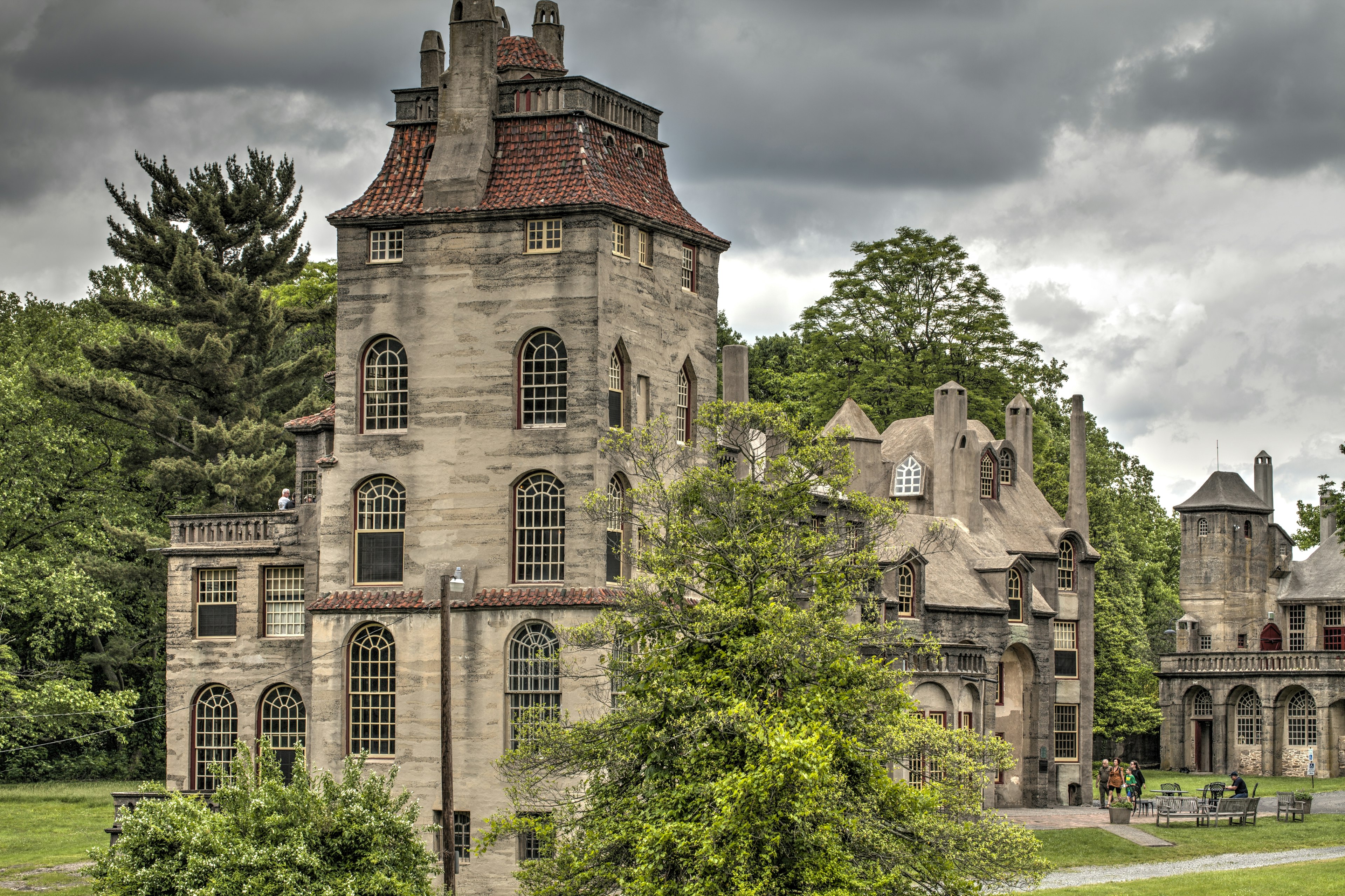 A grey castle with a tall turret and red-tile roof in vast grounds