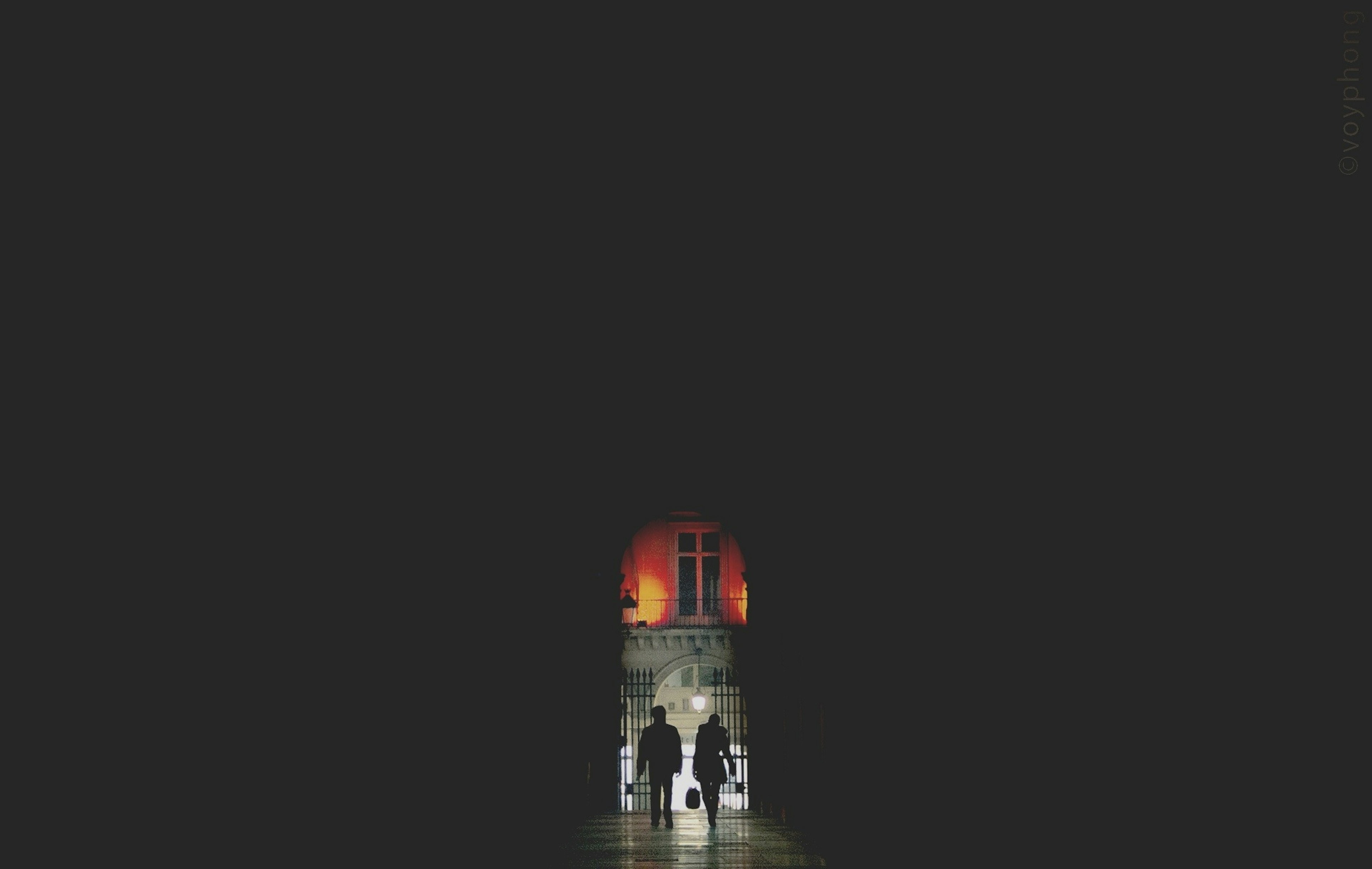 A silhouetted couple walk out of a dark passageway in Paris France and into the night, which is lit up