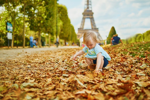 Adorable toddler girl walking on fallen autumn leaves near the Eiffel tower