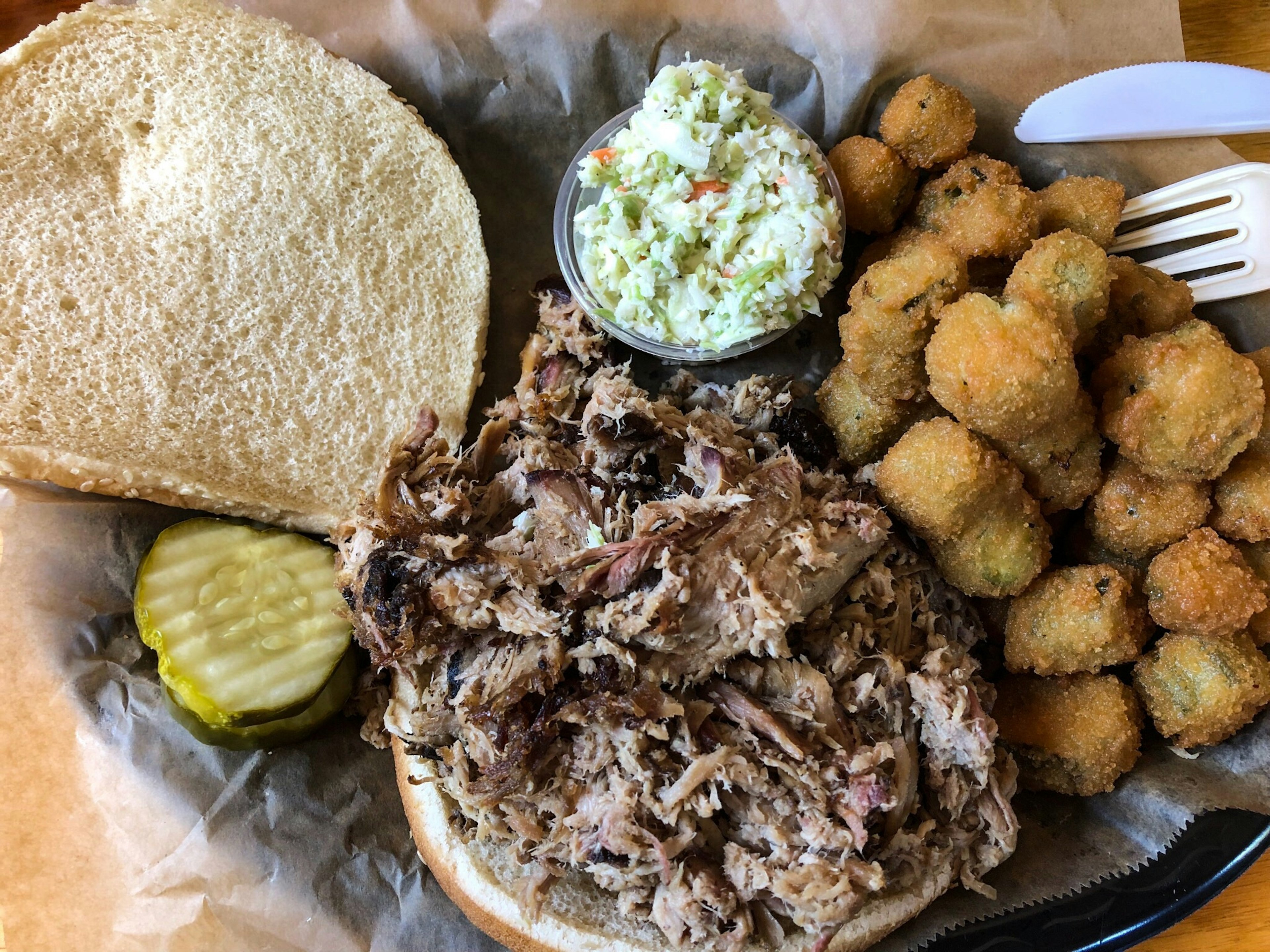 A plateful with a chopped pork barbecue sandwich with cole slaw, pickles, and fried okra