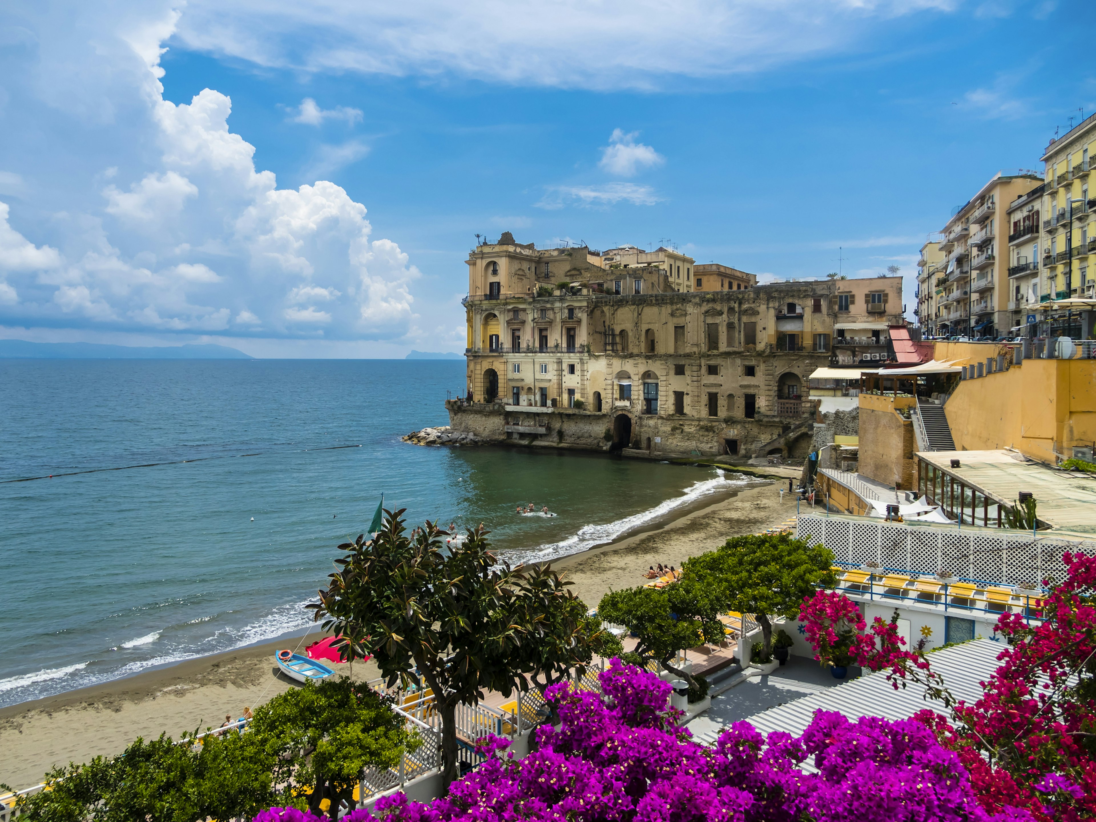 A large coastal palace building with adjacent sandy beach and calm seas