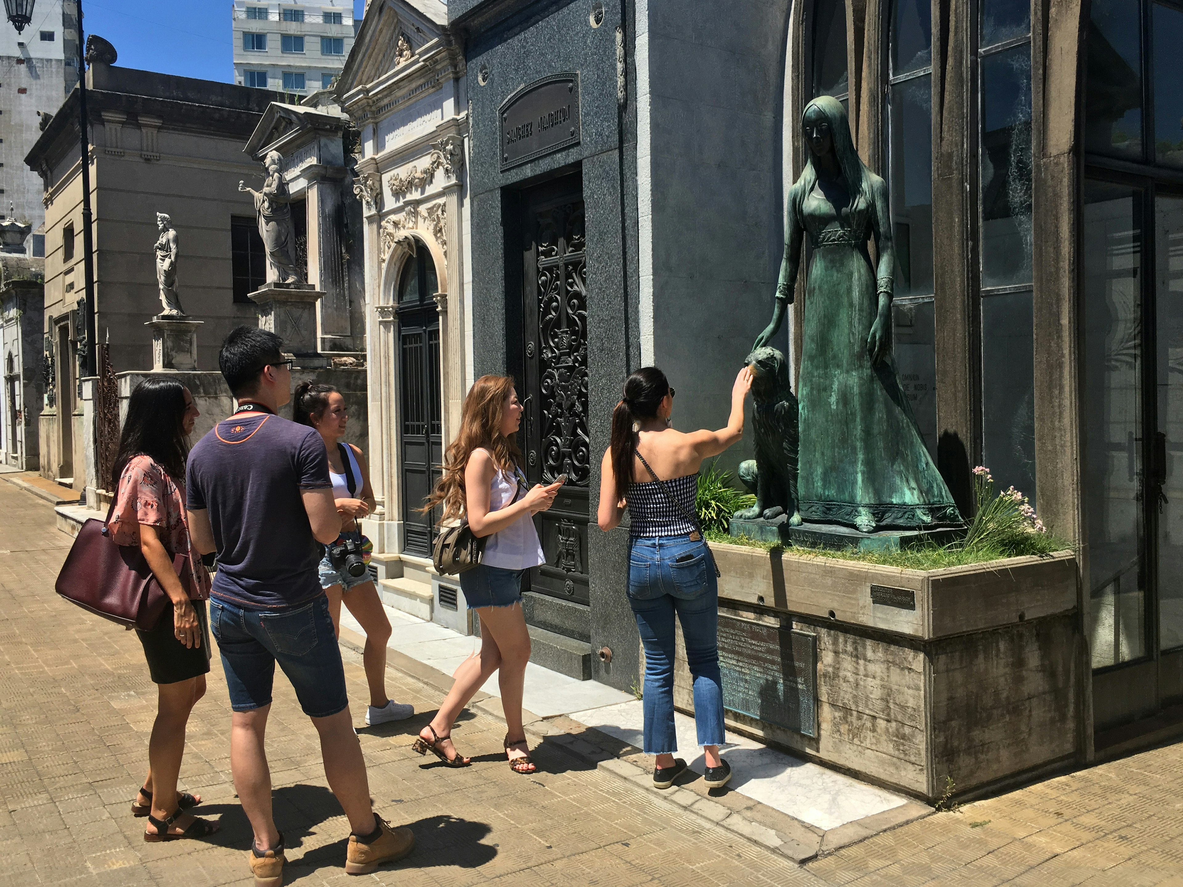 Group of young tourists looking at beautiful statue belonging to mausoleum in Recoleta Cemetery., Buenos Aires.