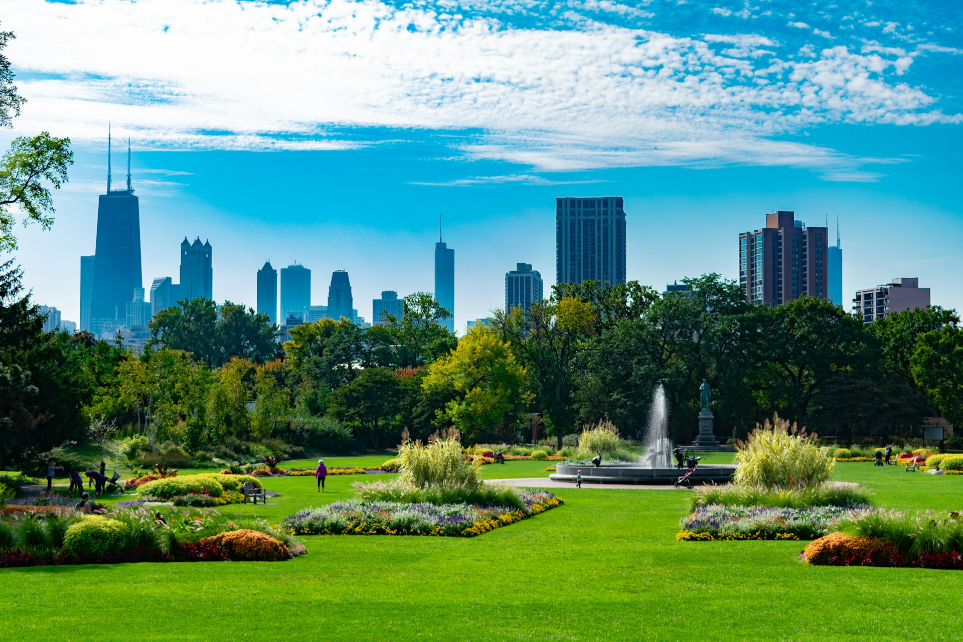 A large garden scene with plants and a fountain in Lincoln Park, Chicago, with the city skyline towering beyond