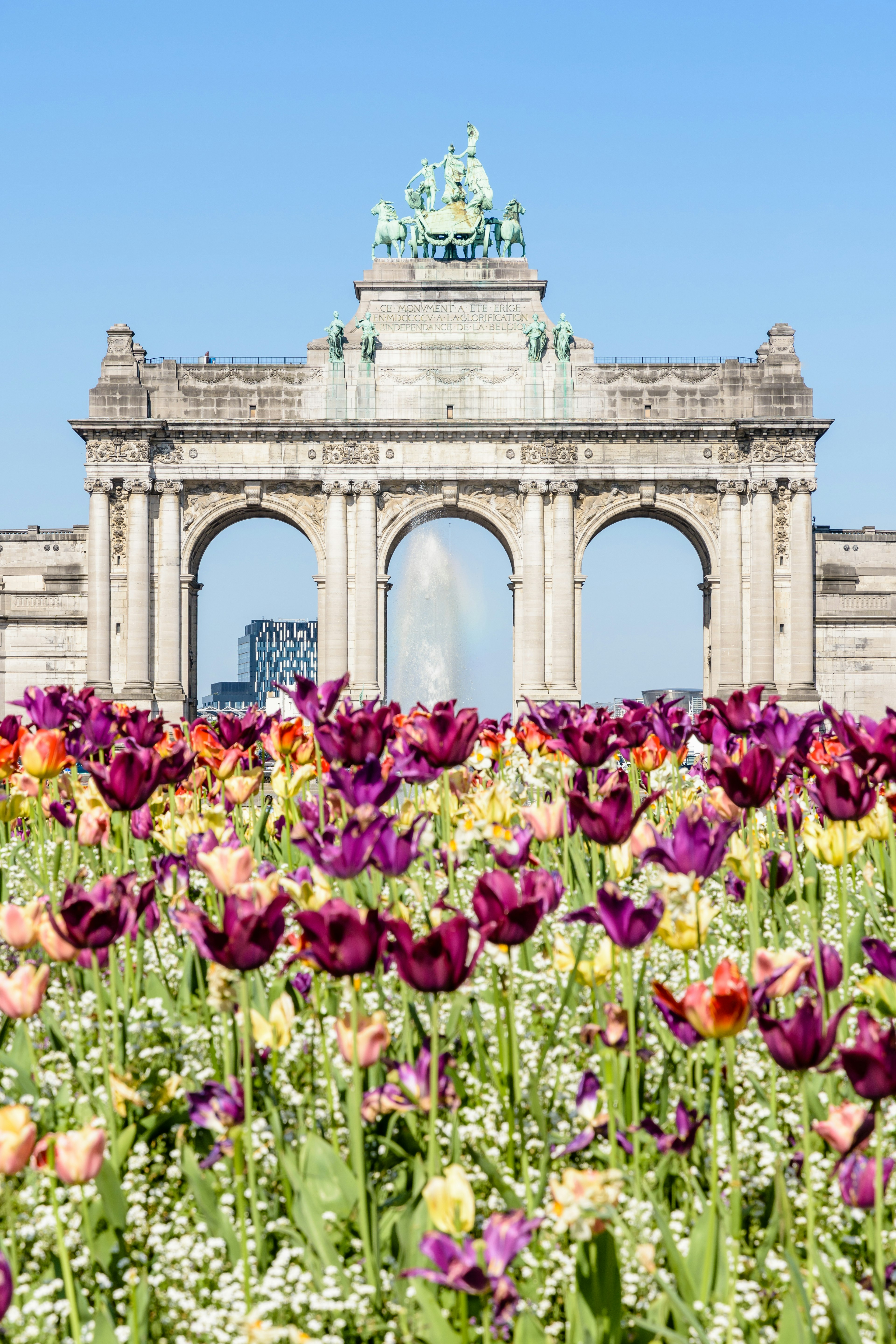 The arcade du Cinquantenaire in Brussels, Belgium, on a sunny day with flowers in the foreground.