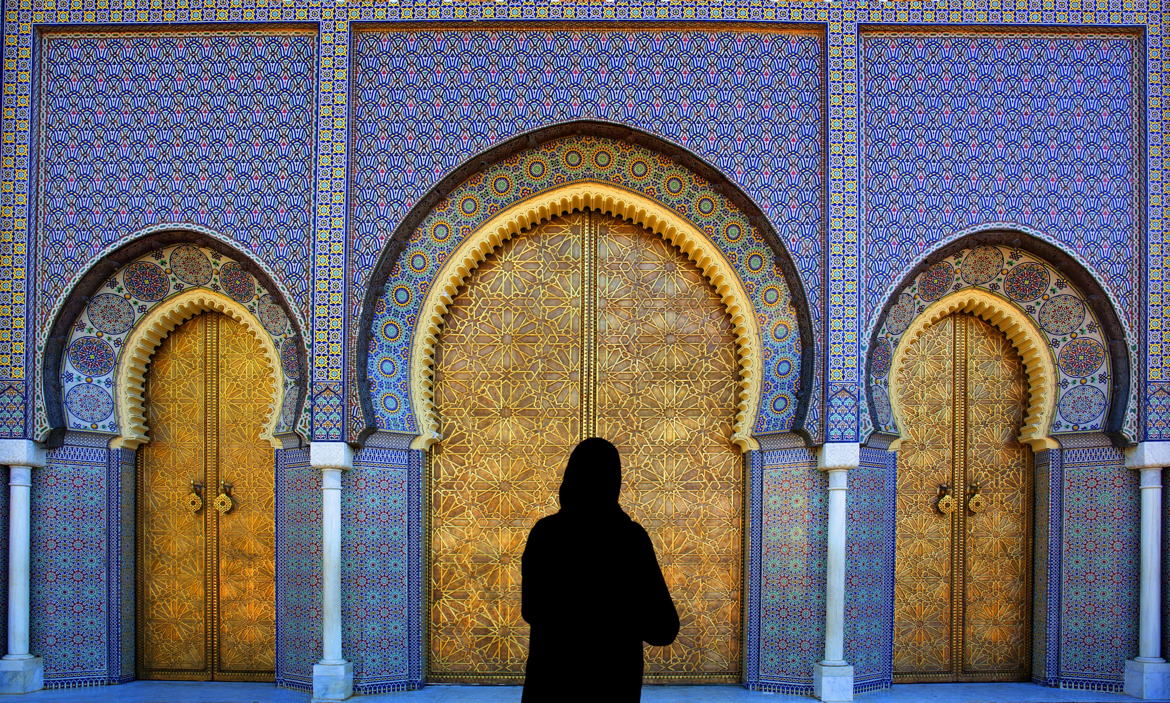 A woman in black stands in front of ornately decorated doors in Fez, Morocco