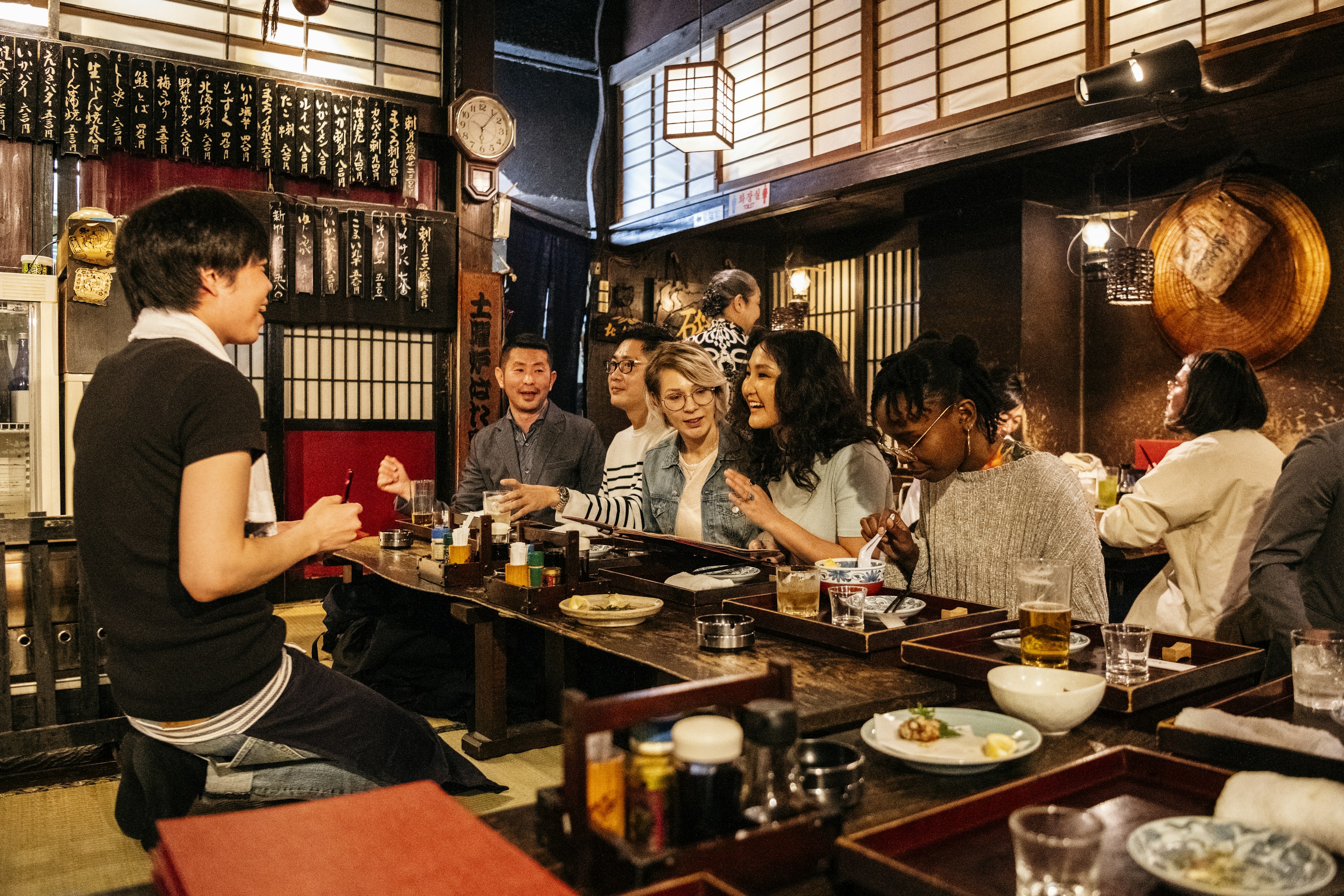 A multiethnic group of friends ordering food at a counter in a Japanese Izakaya