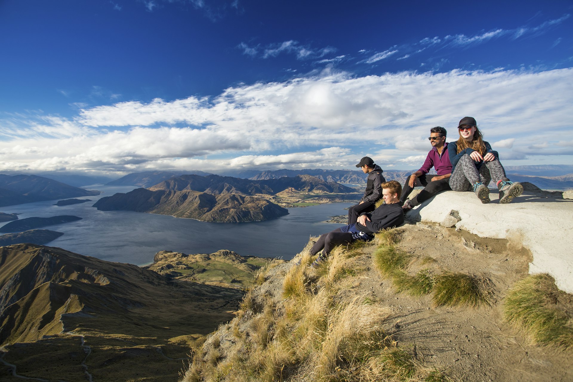 A group of four hikers rests after the strenuous hike to the top of Roy’s Peak, which has gorgeous views of Lake Wanaka below