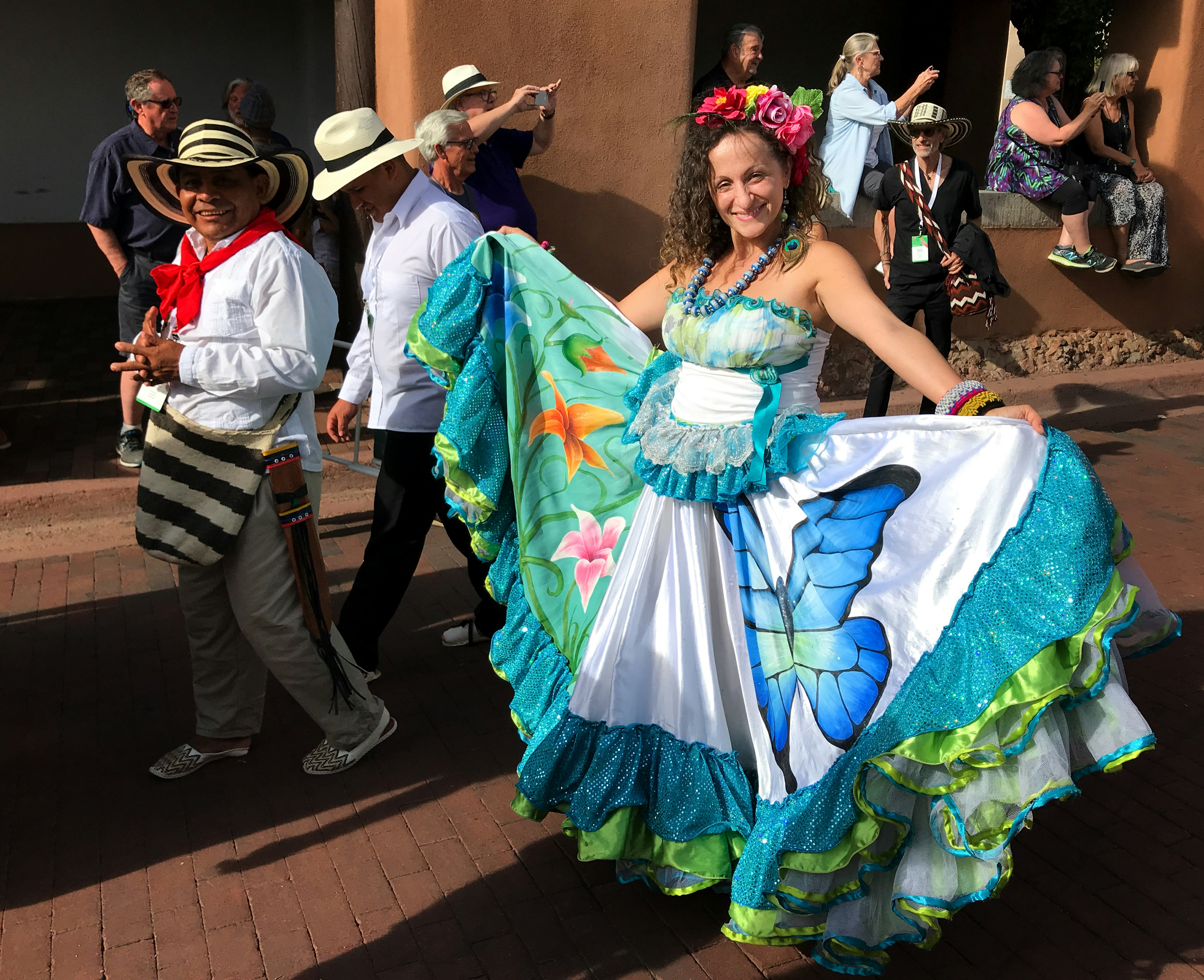 A woman smiles at the camera as she parades down a street. She's wearing a beautiful dress with intricate designs, which she proudly shows to the camera