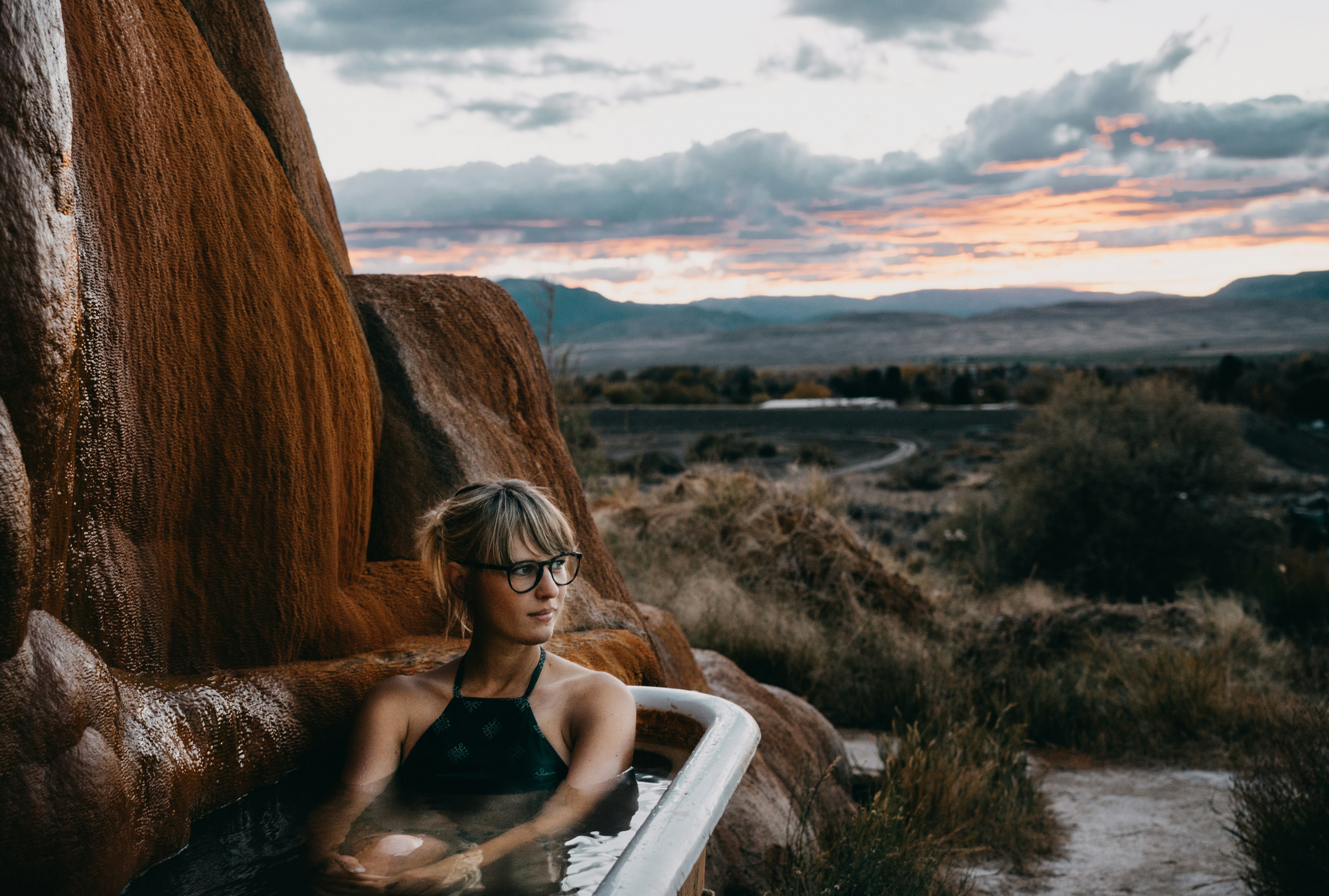 Женщина сидит в ванной с горячими источниками на Mystic Hot Springs в Юте во время заката