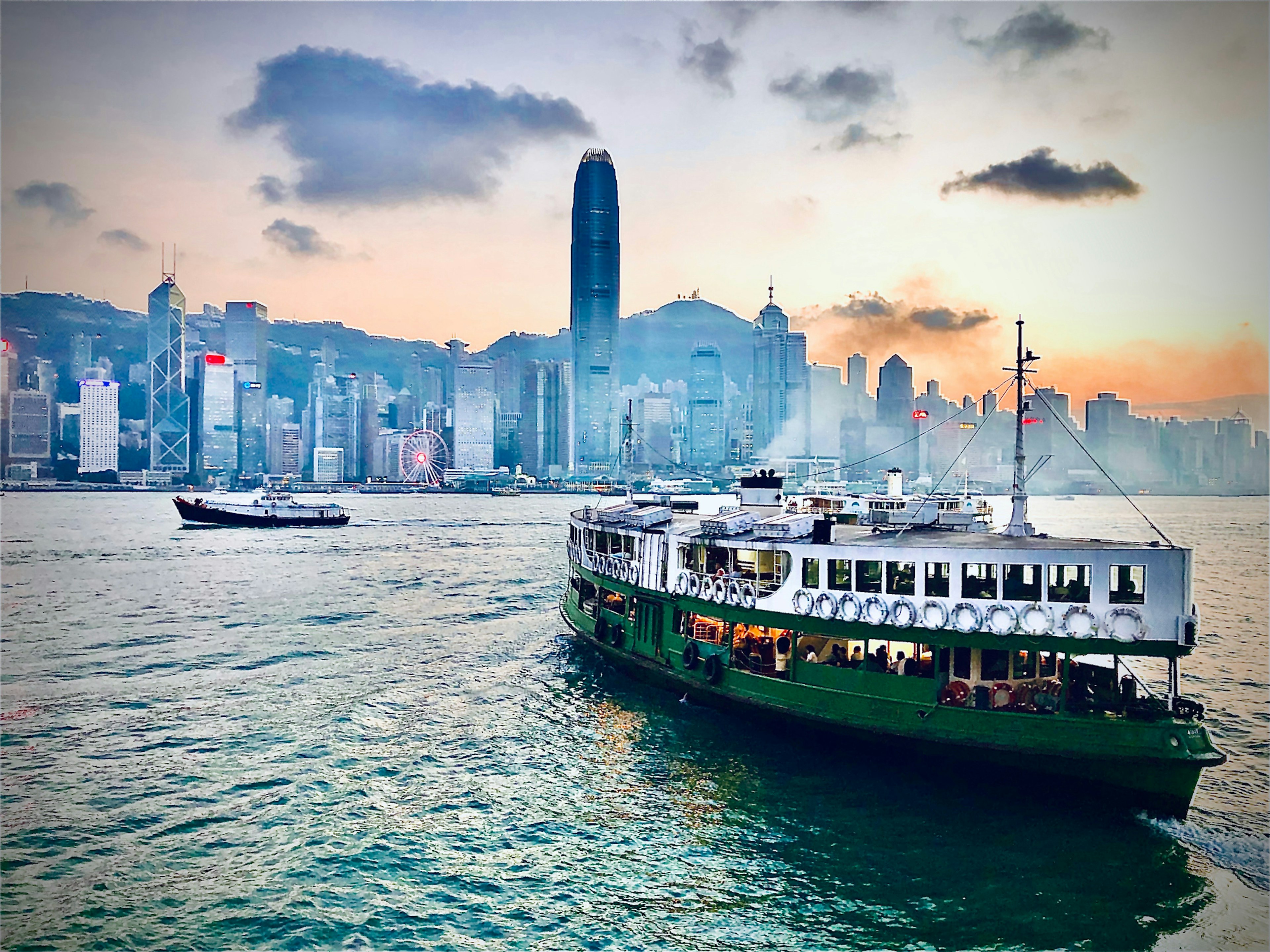 The Star Ferry in Victoria Harbour, Hong Kong goes across the water towards skyscrapers at sunset