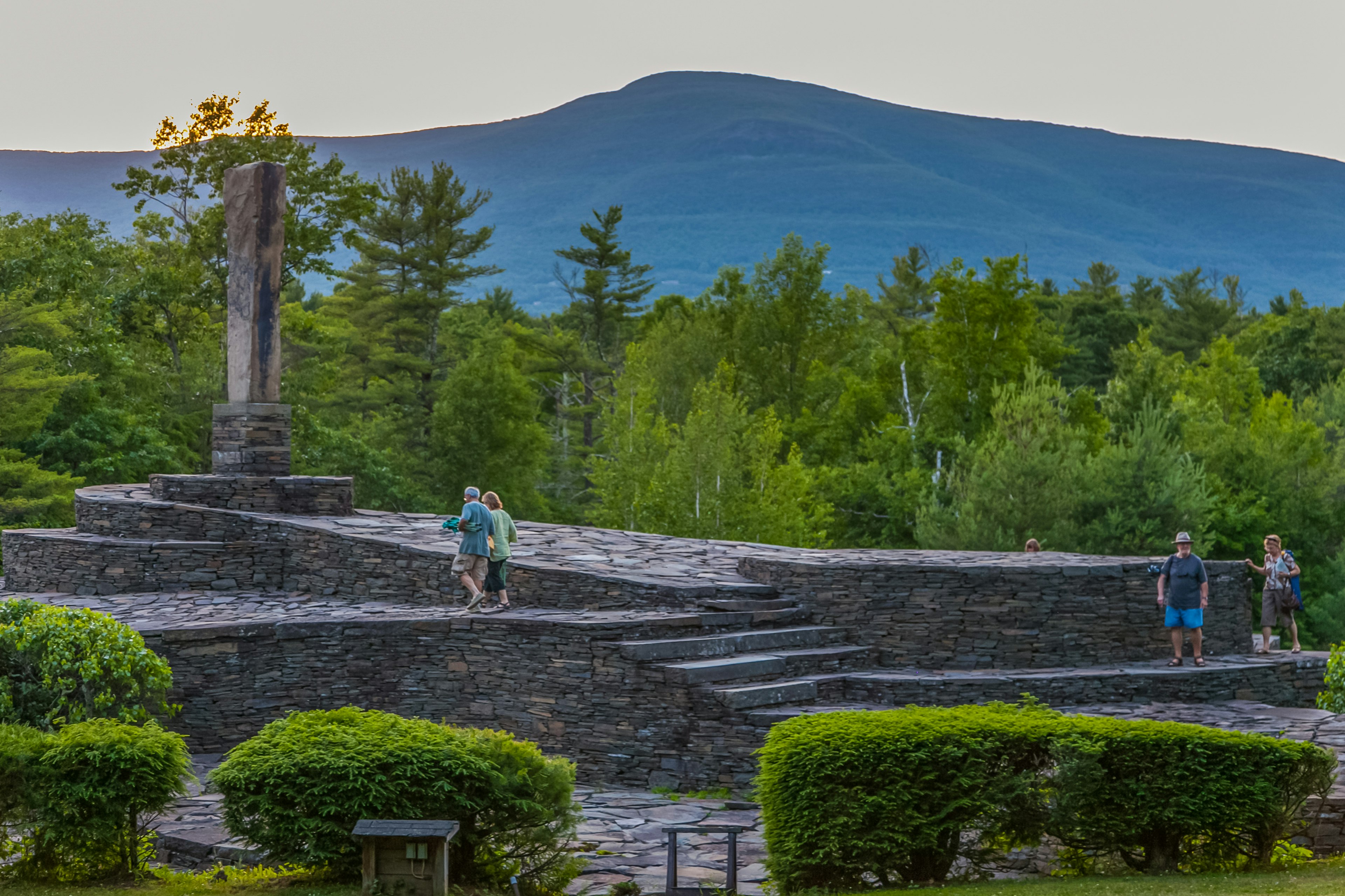 Tourists wander around an outdoor sculpture garden with a huge central stone obelisk