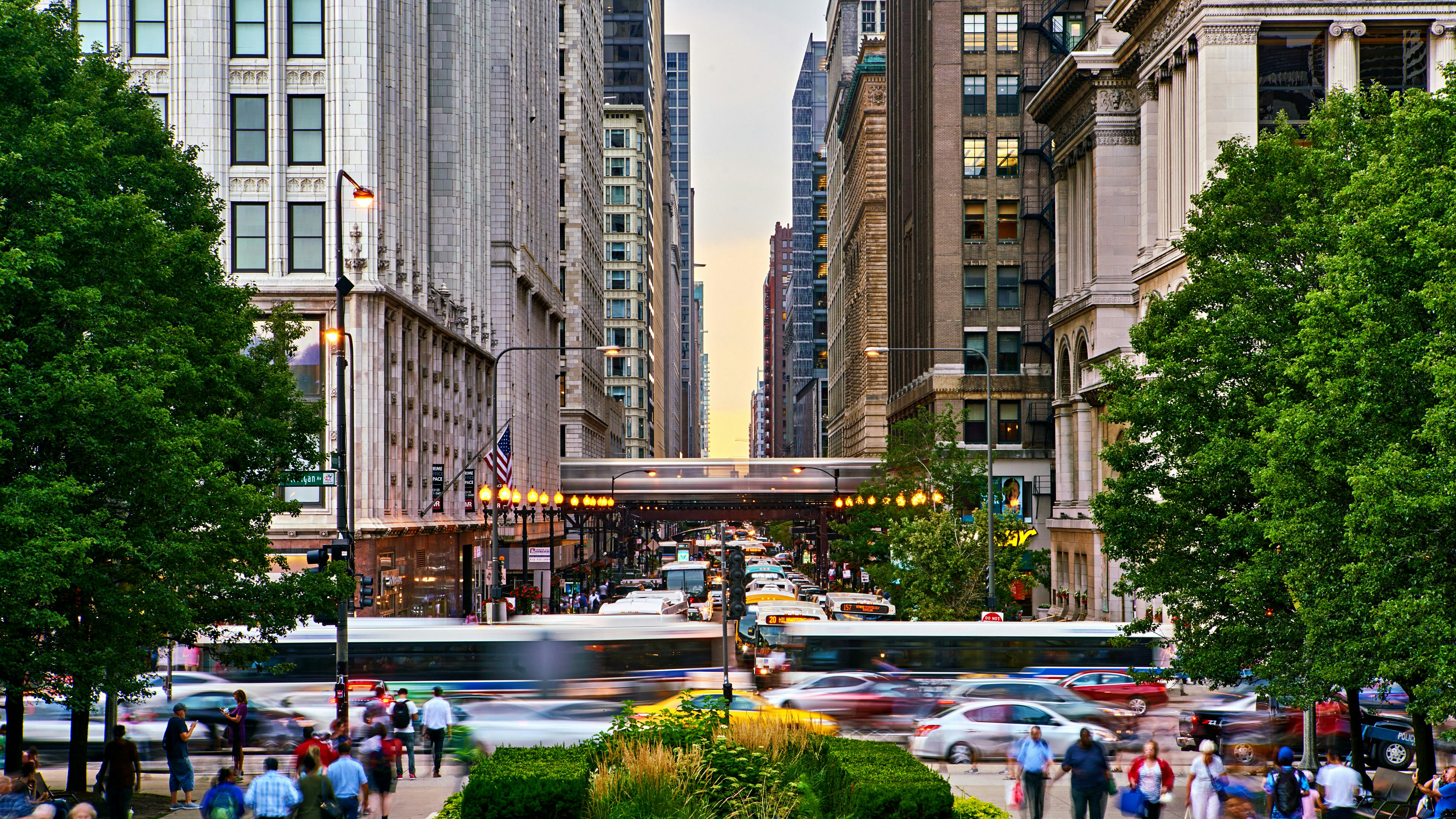 Pedestrians walk the streets of Chicago while buses and the L whiz by, blurred by motion