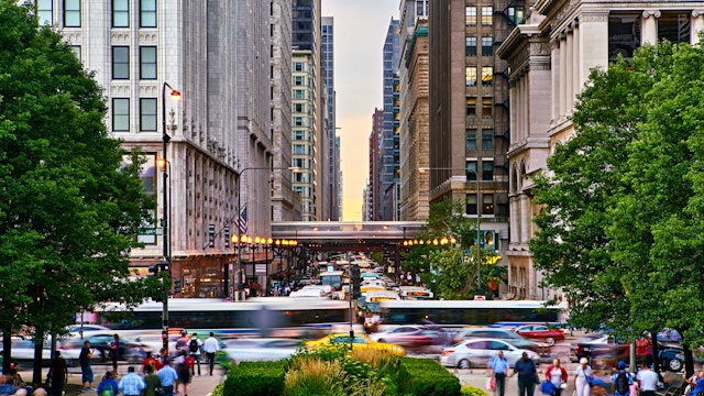 Pedestrians walk the streets of Chicago while buses and the L whiz by, blurred by motion