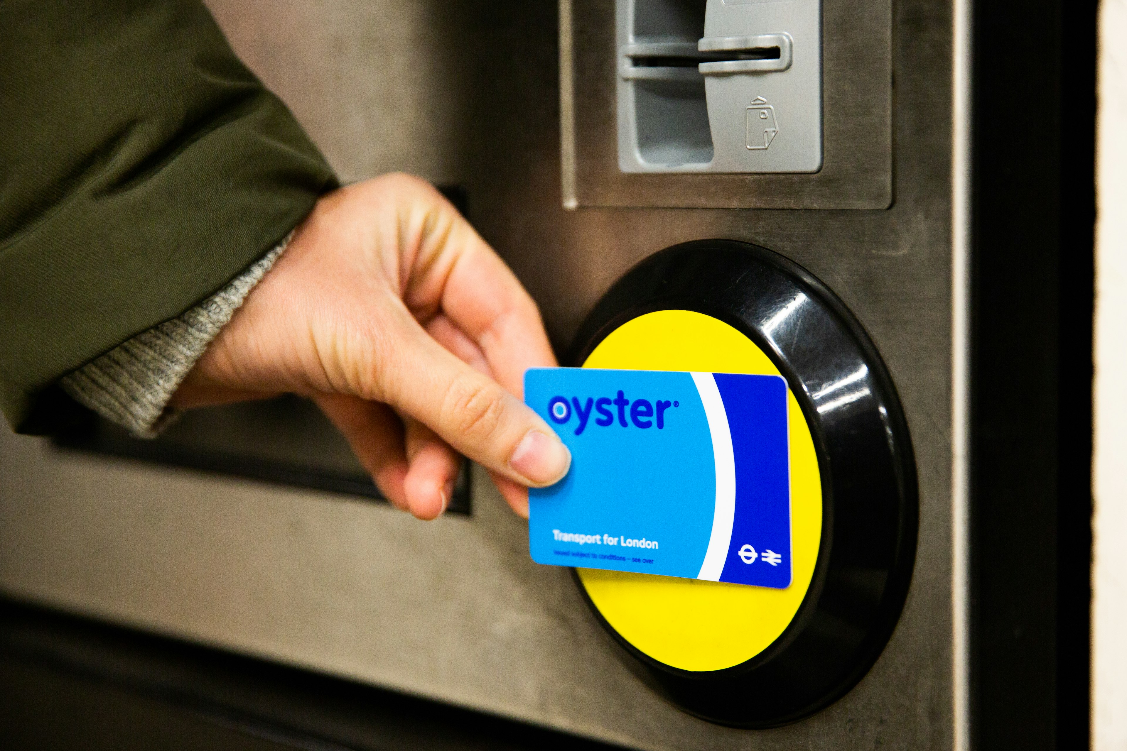 Female hand holding a blue Oyster card, touching yellow pad on automatic ticket barriers