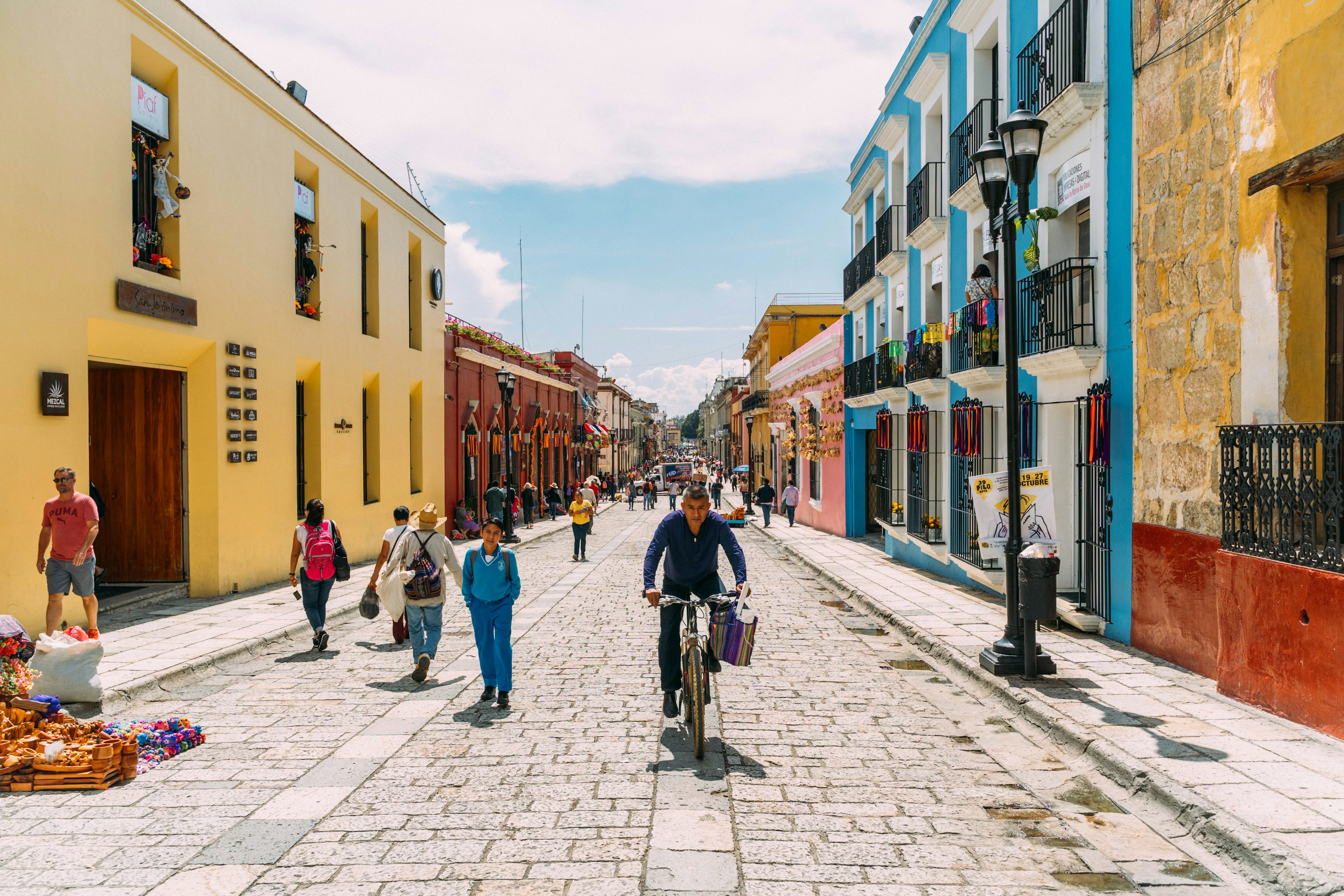 People walking, cycling and selling souvenirs on a colorful pedestrian stree in Oaxaca