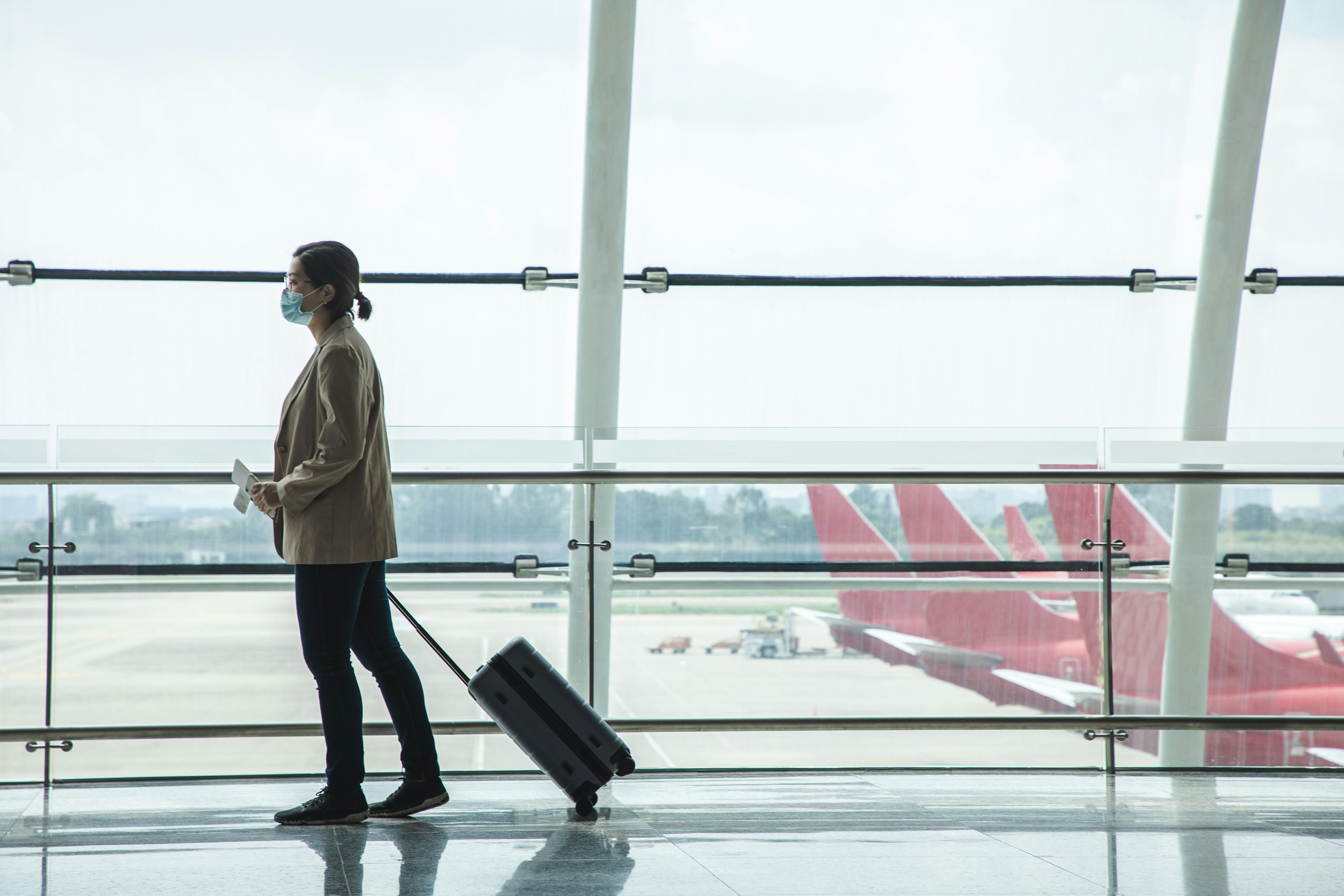 Asian businesswoman wearing a mask at the airport with passport and airplane ticket in her hand