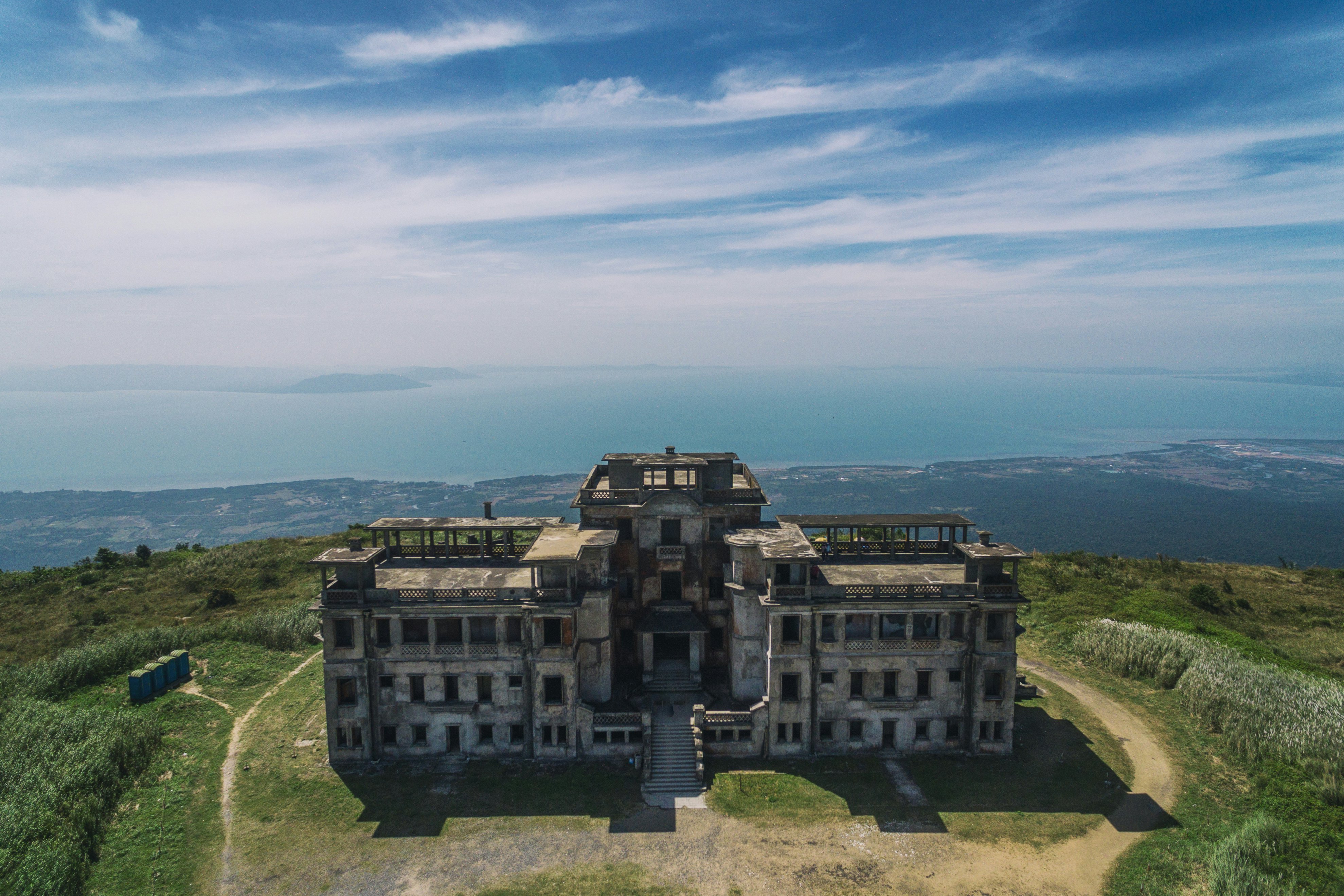 A ruined French colonial-era building at the top of a hill in Cambodia; there is a view of the sea far below.