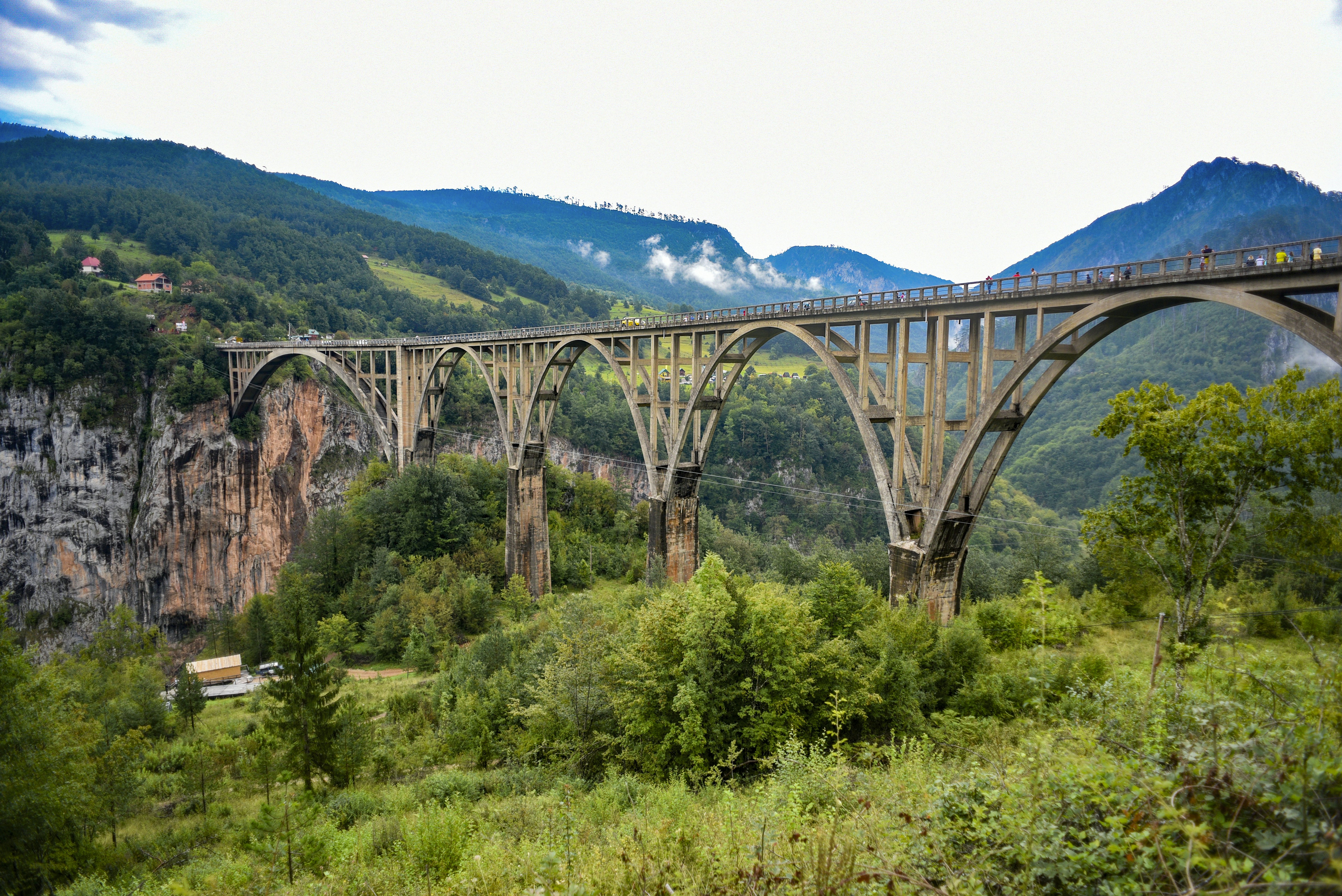 People walk over a multi-arched bridge spanning a gorge in a mountainous area