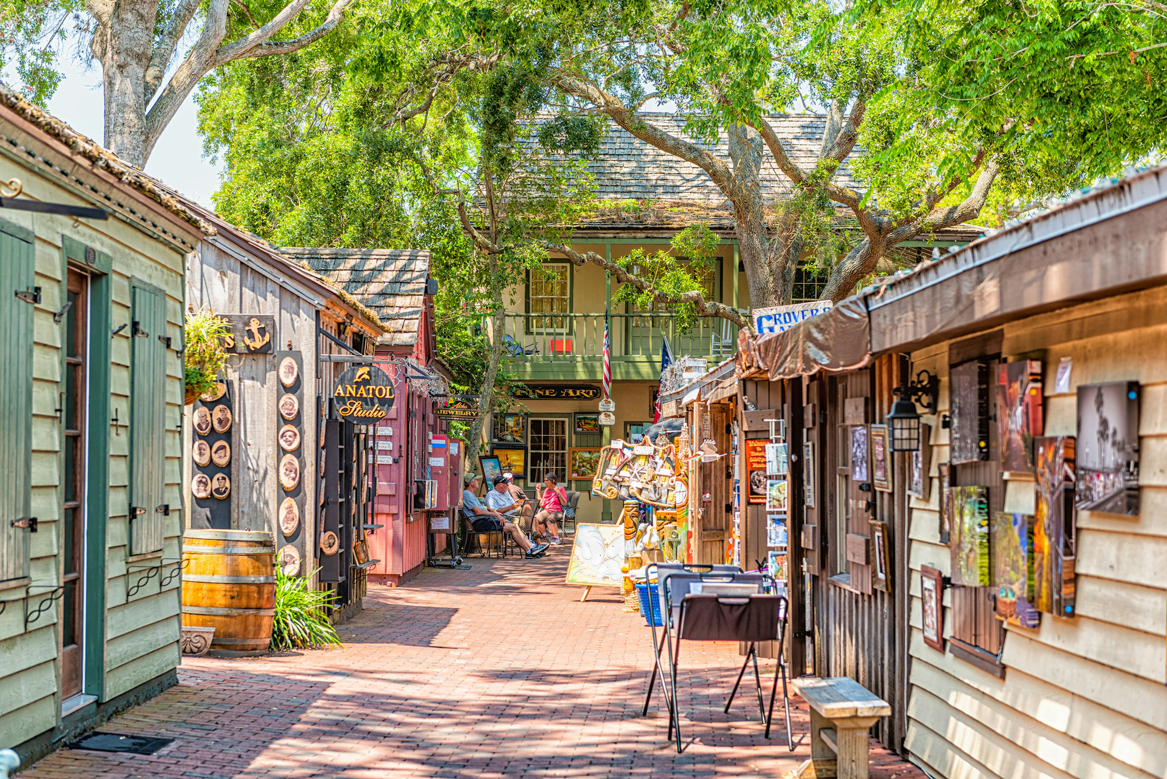 A quaint narrow street lined with small huts selling arts and crafts; vendors are seated at the end of the path