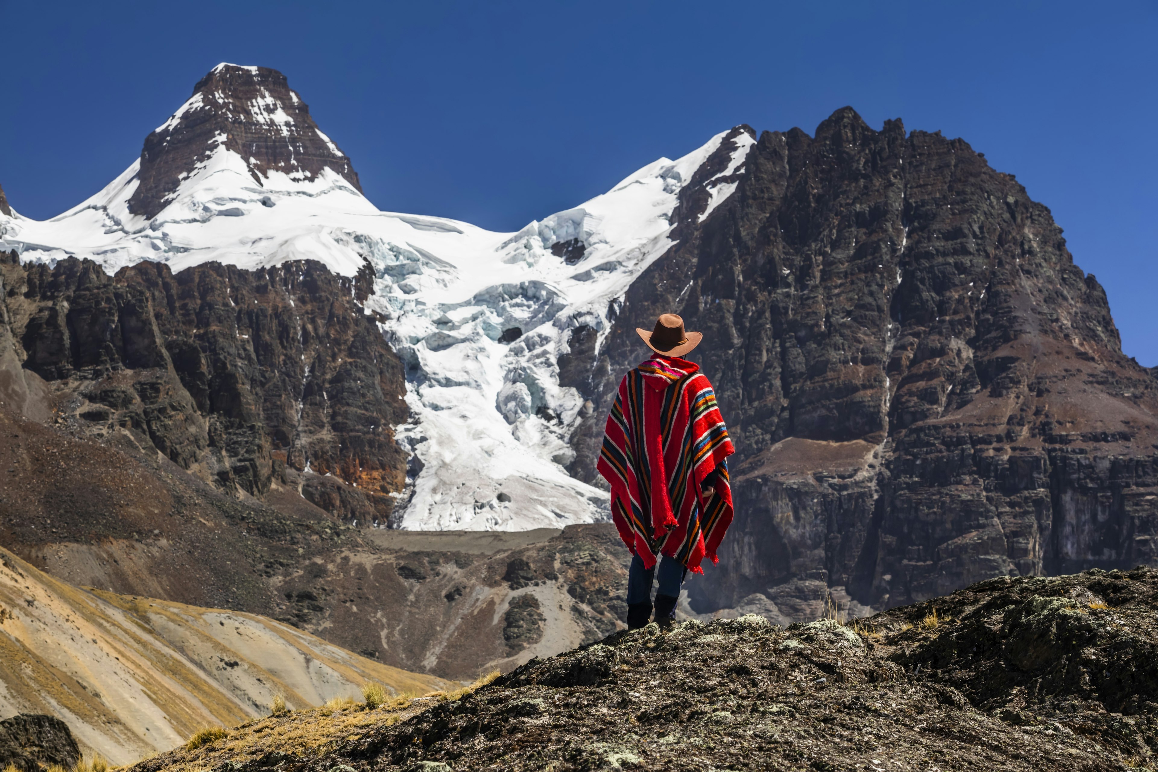 A hiker in a poncho in front of a mountain peak