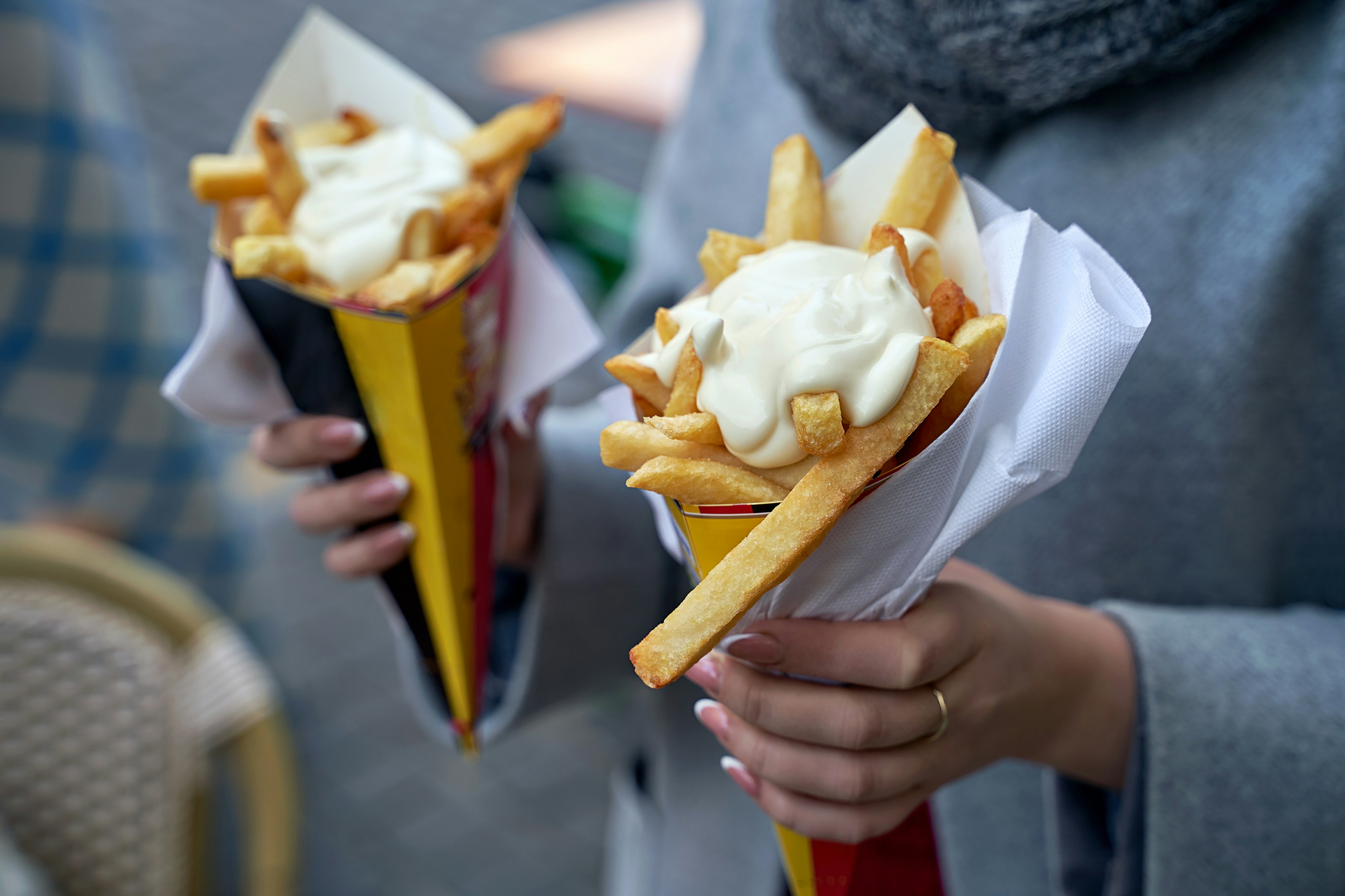 A woman holds two traditional paper cones filled with fries that are topped with mayonnaise.