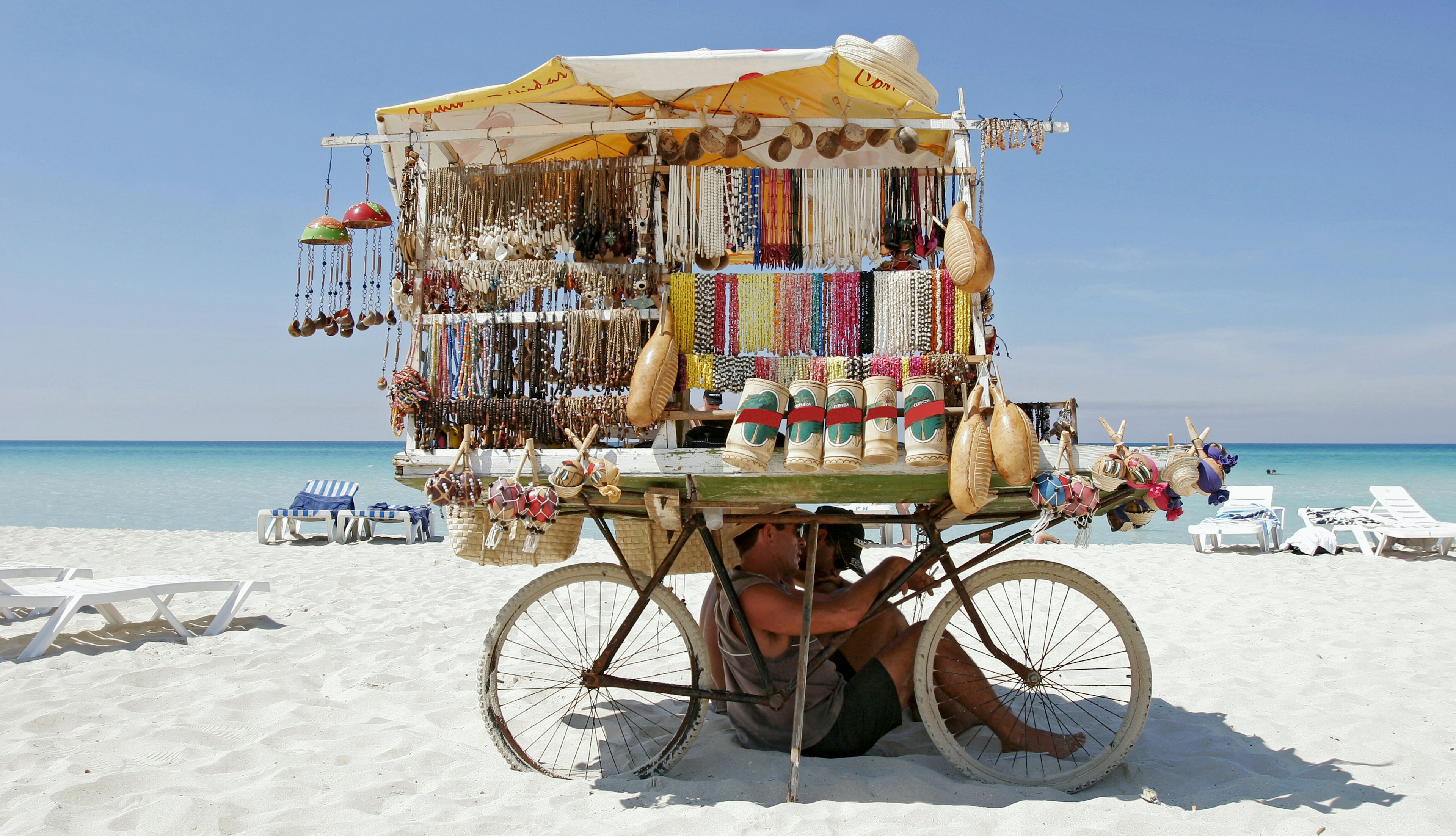 souvenir vendors taking shade under bicycle stall on beach