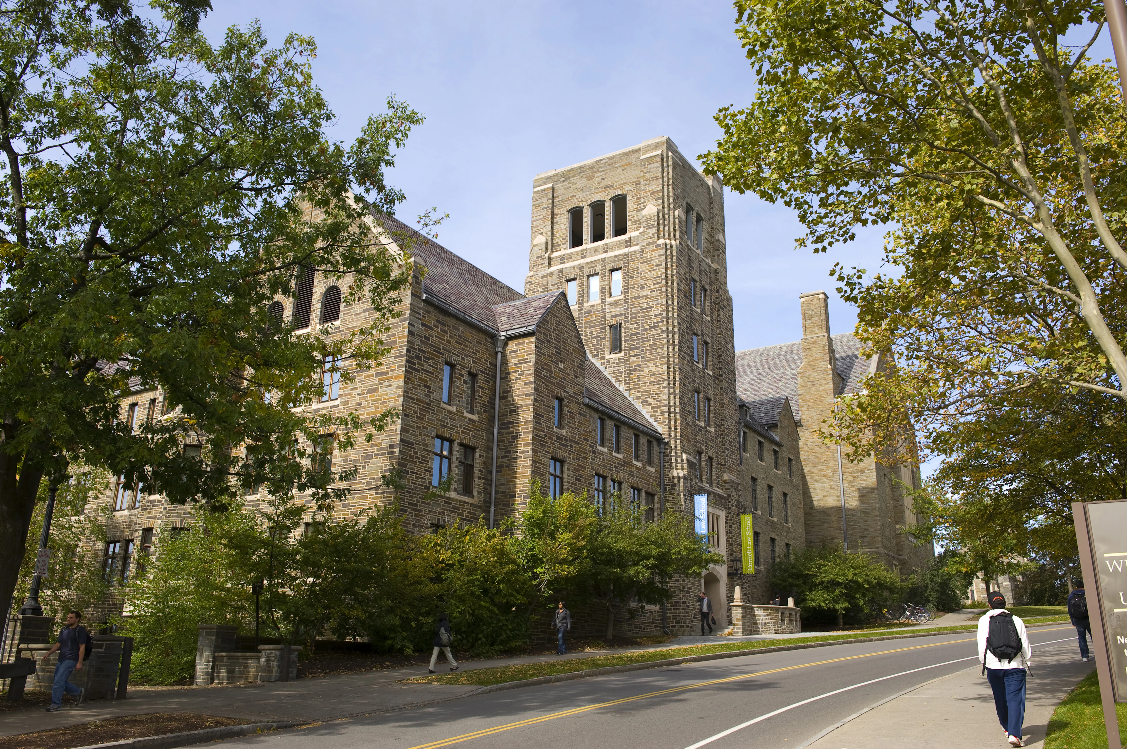 Студент идет рядом с большими зданиями кампуса Университета Корнелла