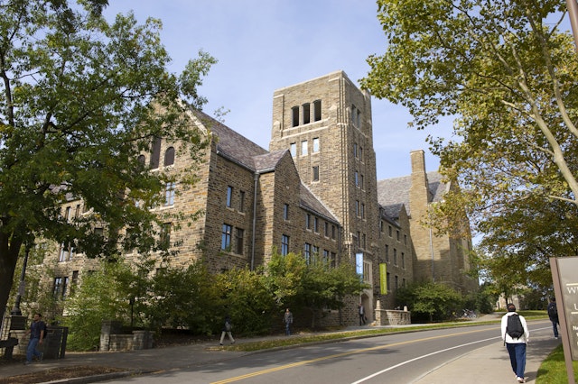 A student walks next to large buildings on the campus of Cornell University