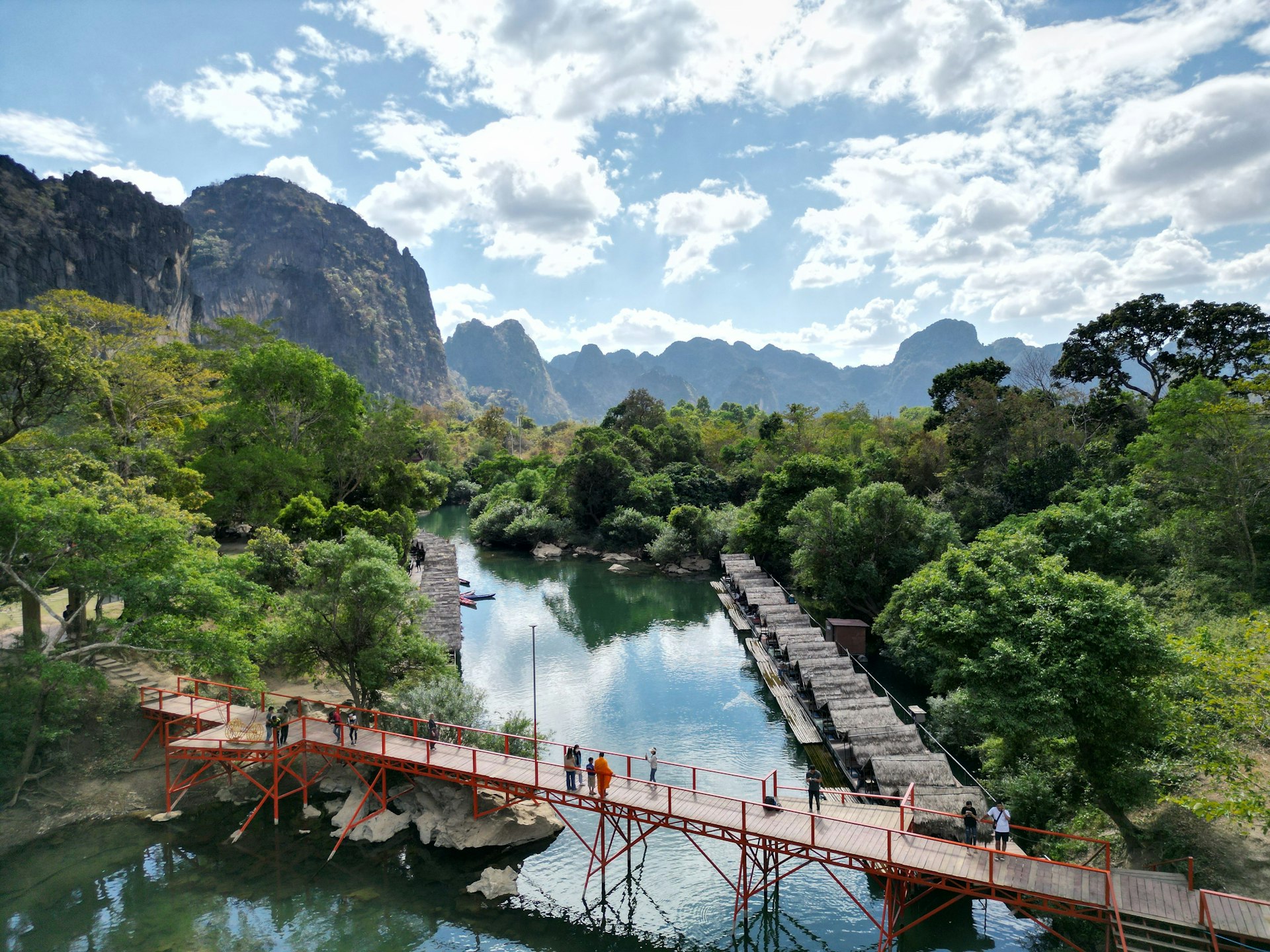 An aerial view of a bridge over the water near a majestic mountain range in Tha Khaek Loop, Laos