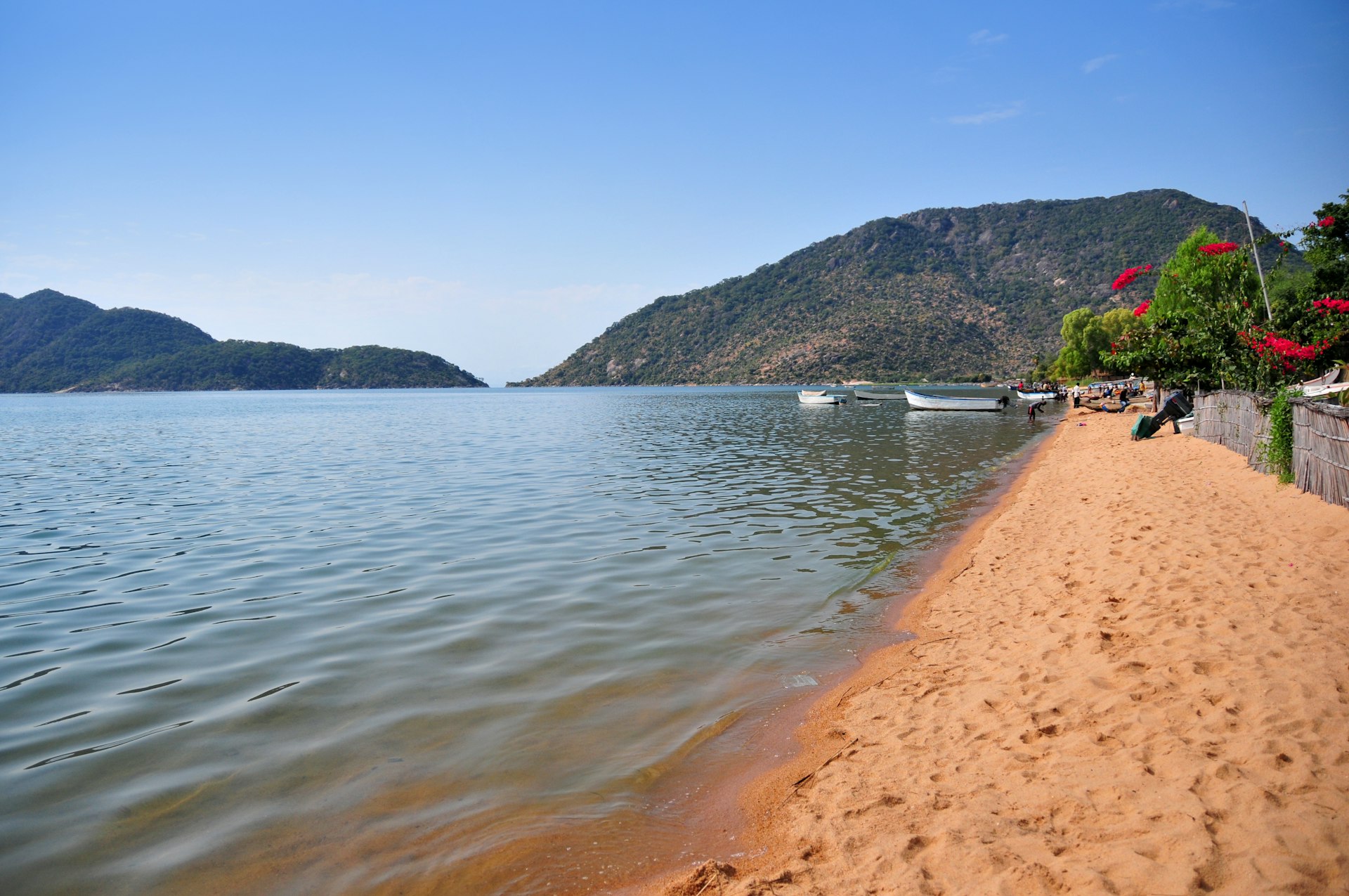 A stretch of golden sand lapped gently by the lakeshore, with boats moored in the distance