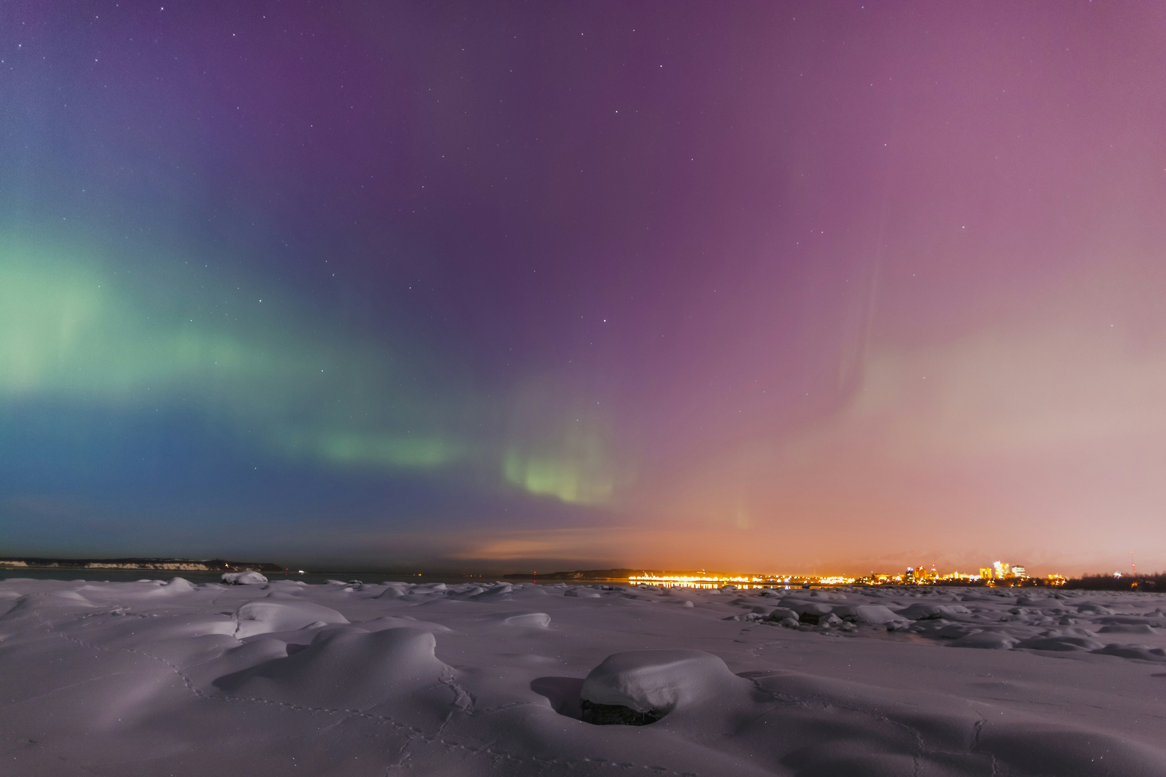 The Northern Lights Shine Above The Anchorage City Skyline In This Nighttime View From The Tony Knowles Coastal Trail In Winter