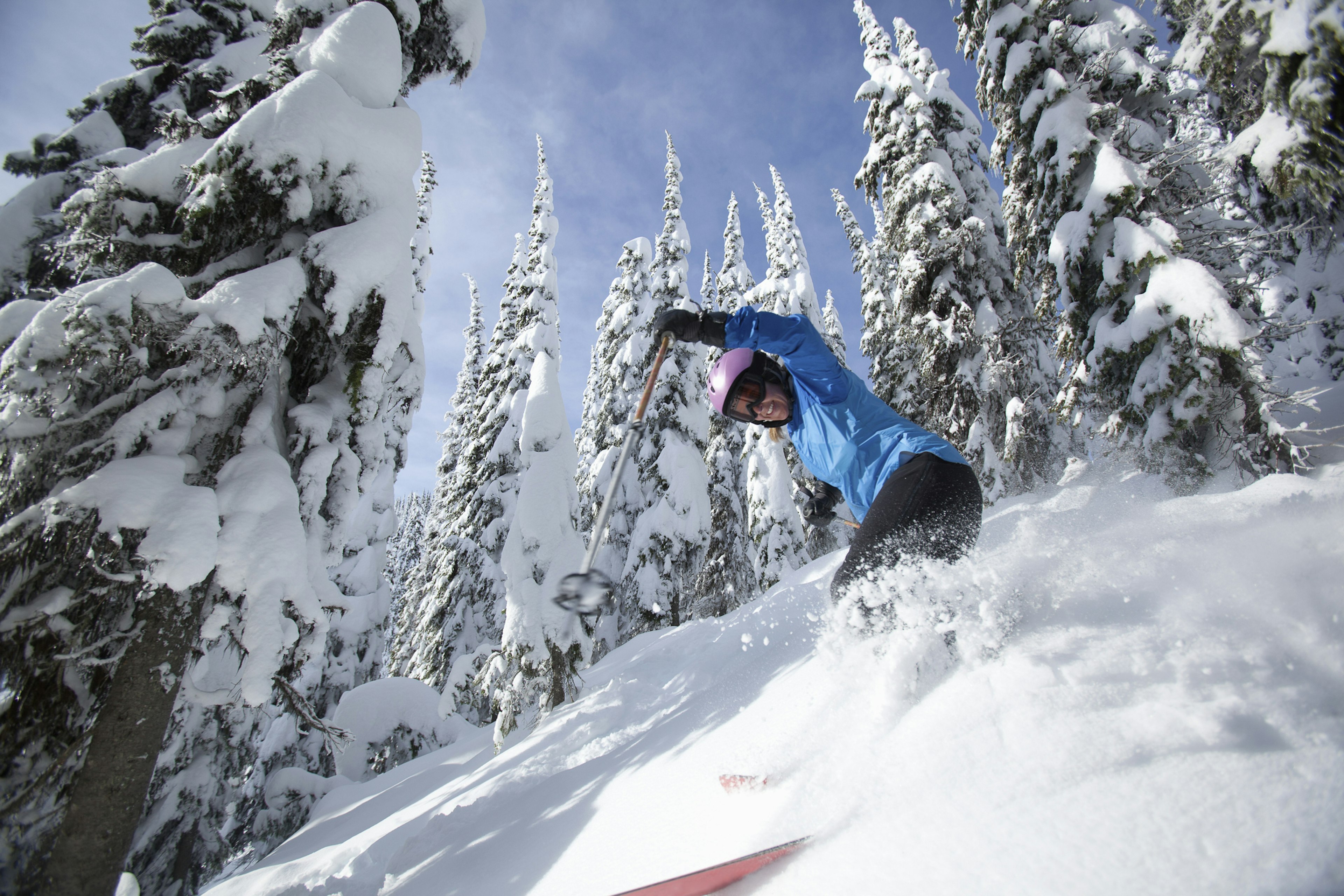 A smiling woman in ski gear comes down a hill covered with deep snow in the backcountry in Montana